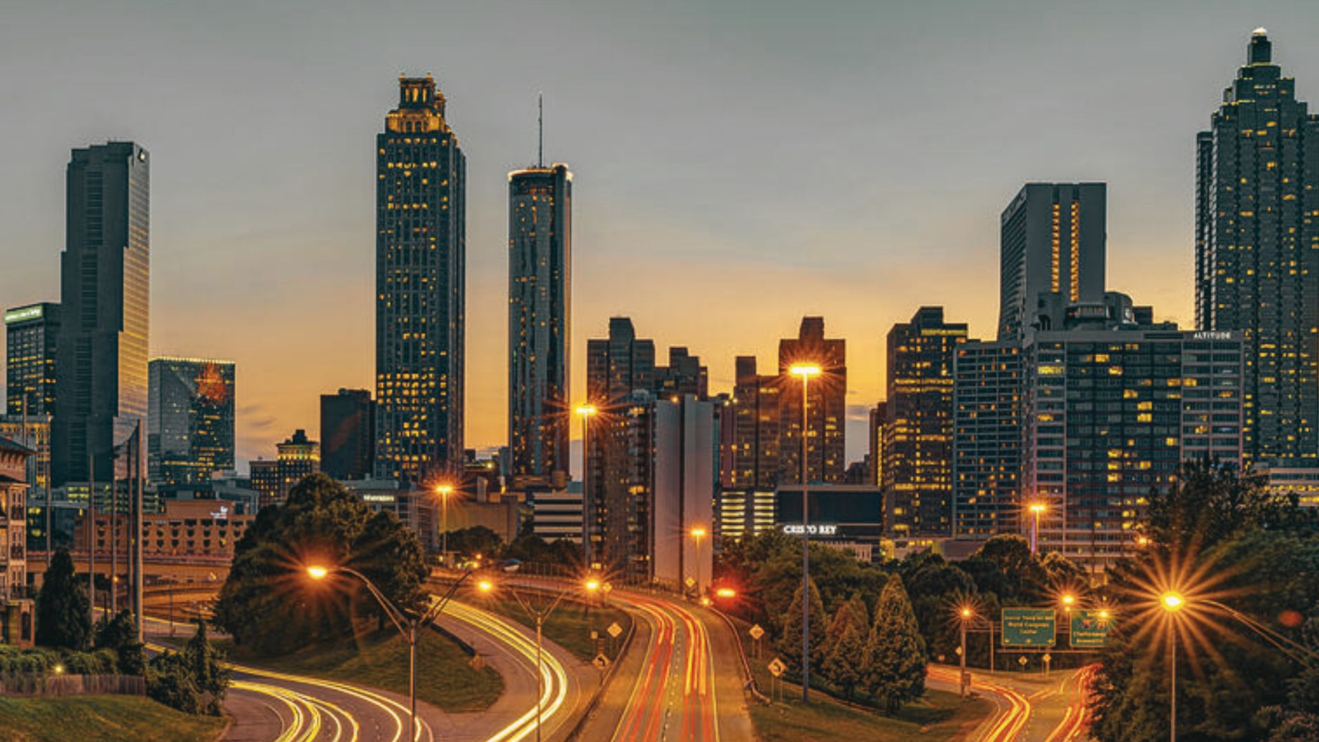 Sunset view from Jackson Street Bridge with Atlanta skyline and glowing traffic along downtown roads.