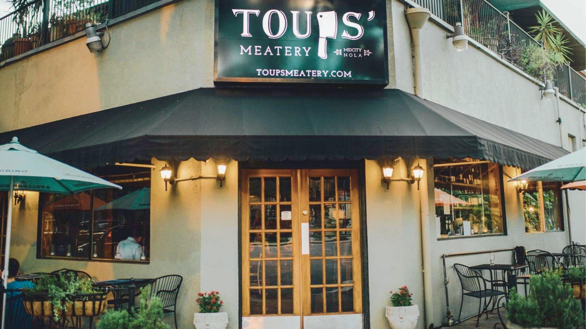 Corner entrance of Toups’ Meatery in Mid-City NOLA with black awnings and outdoor patio seating.