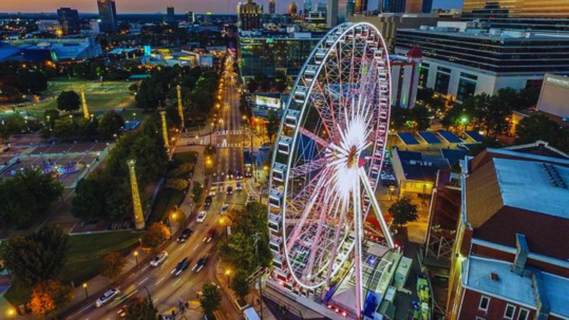SkyView Atlanta Ferris wheel shines above downtown streets and Centennial Olympic Park at dusk in Atlanta.