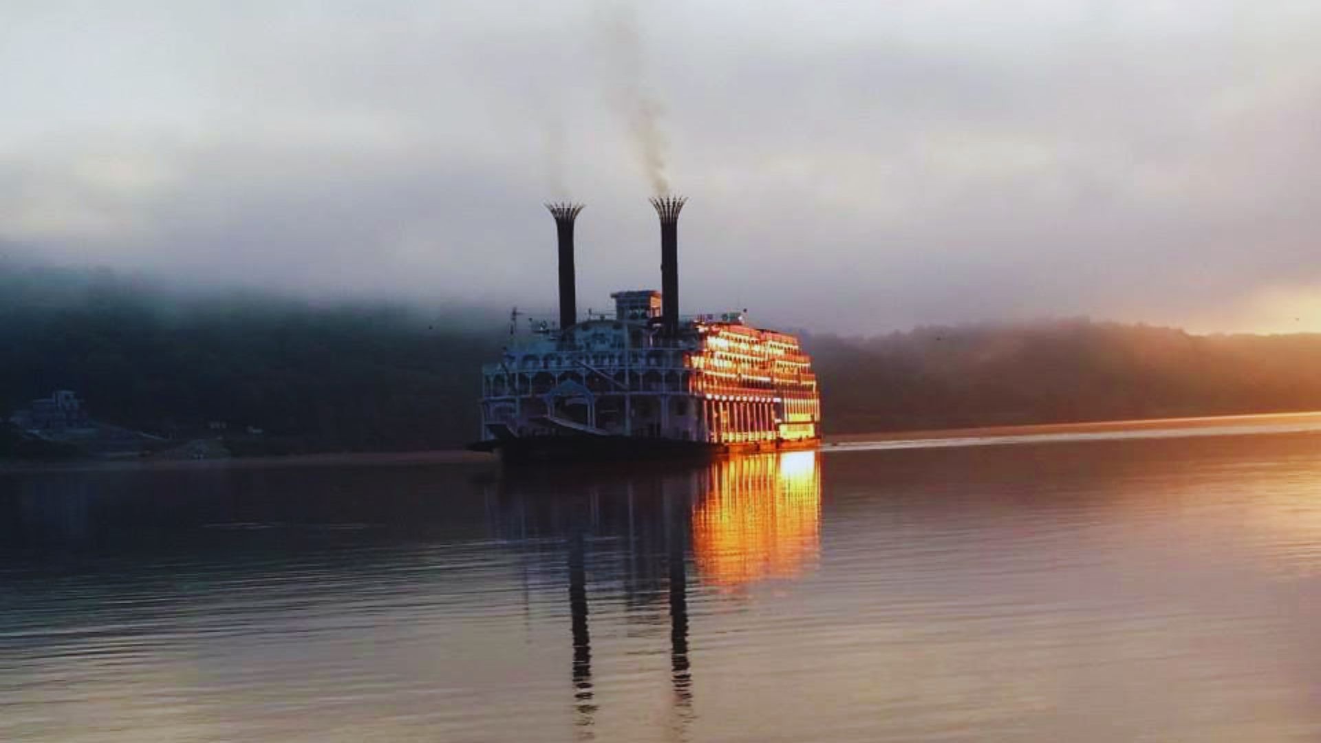 Riverboat glides across the calm riverfront at sunrise.