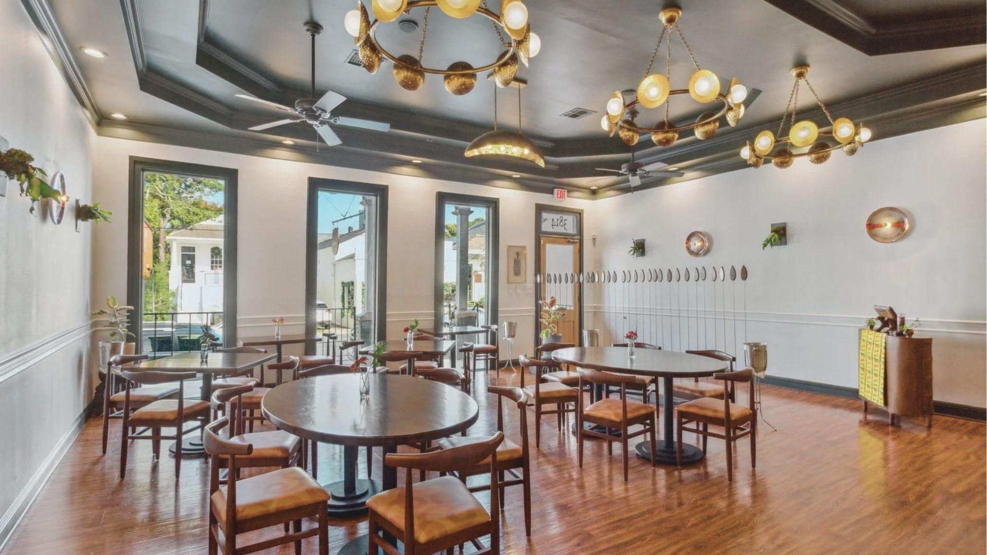 Sunlit modern dining room with dark wood tables, leather chairs, and brass globe chandeliers at a top New Orleans restaurant.