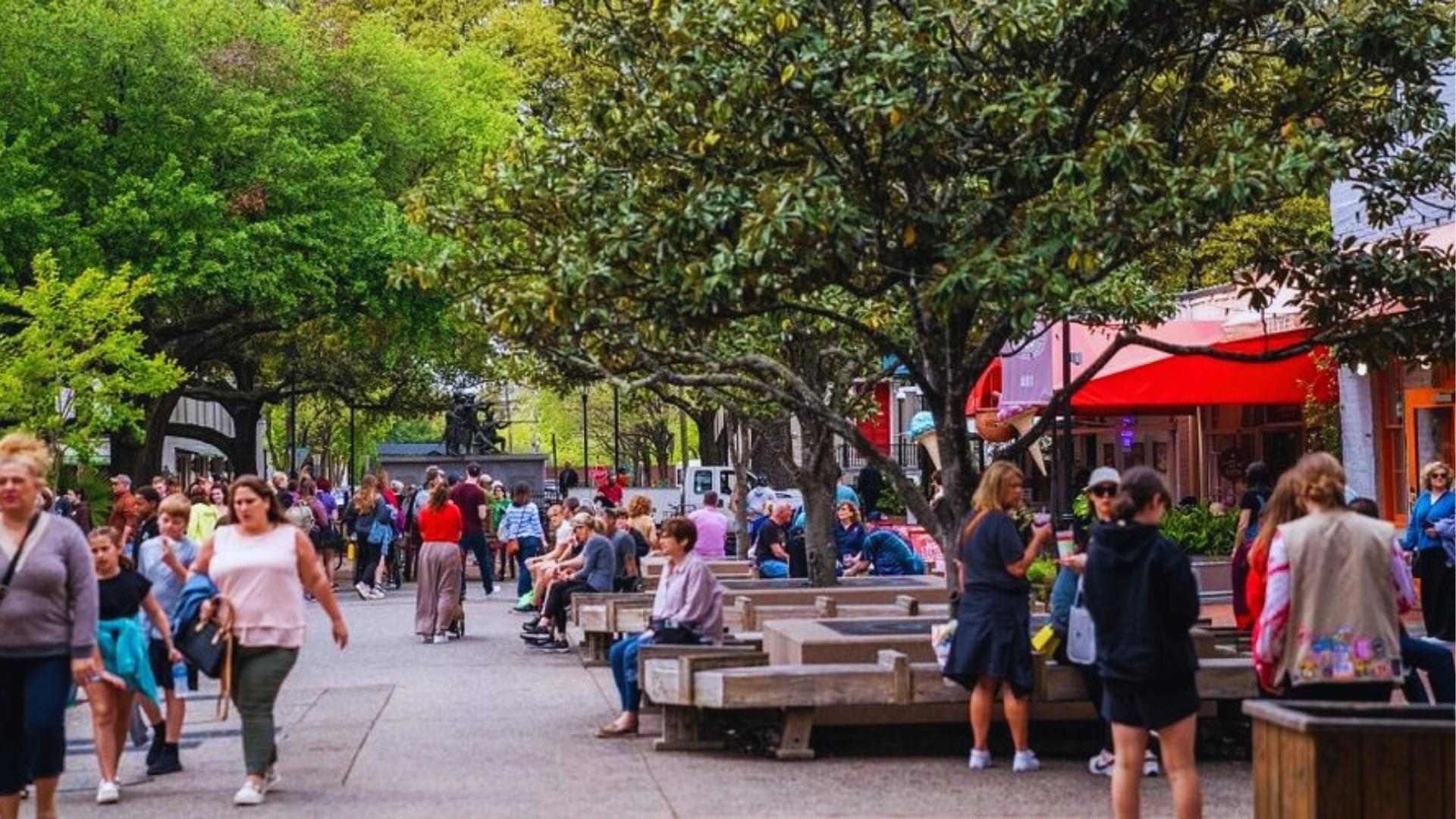 Crowds walking through Savannah City Market with shops and trees on a busy day.