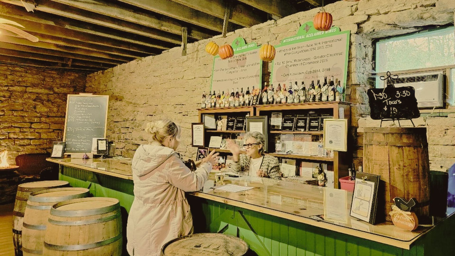 Visitors chat at the Baker Bird Winery tasting counter surrounded by wine bottles and rustic barrels.