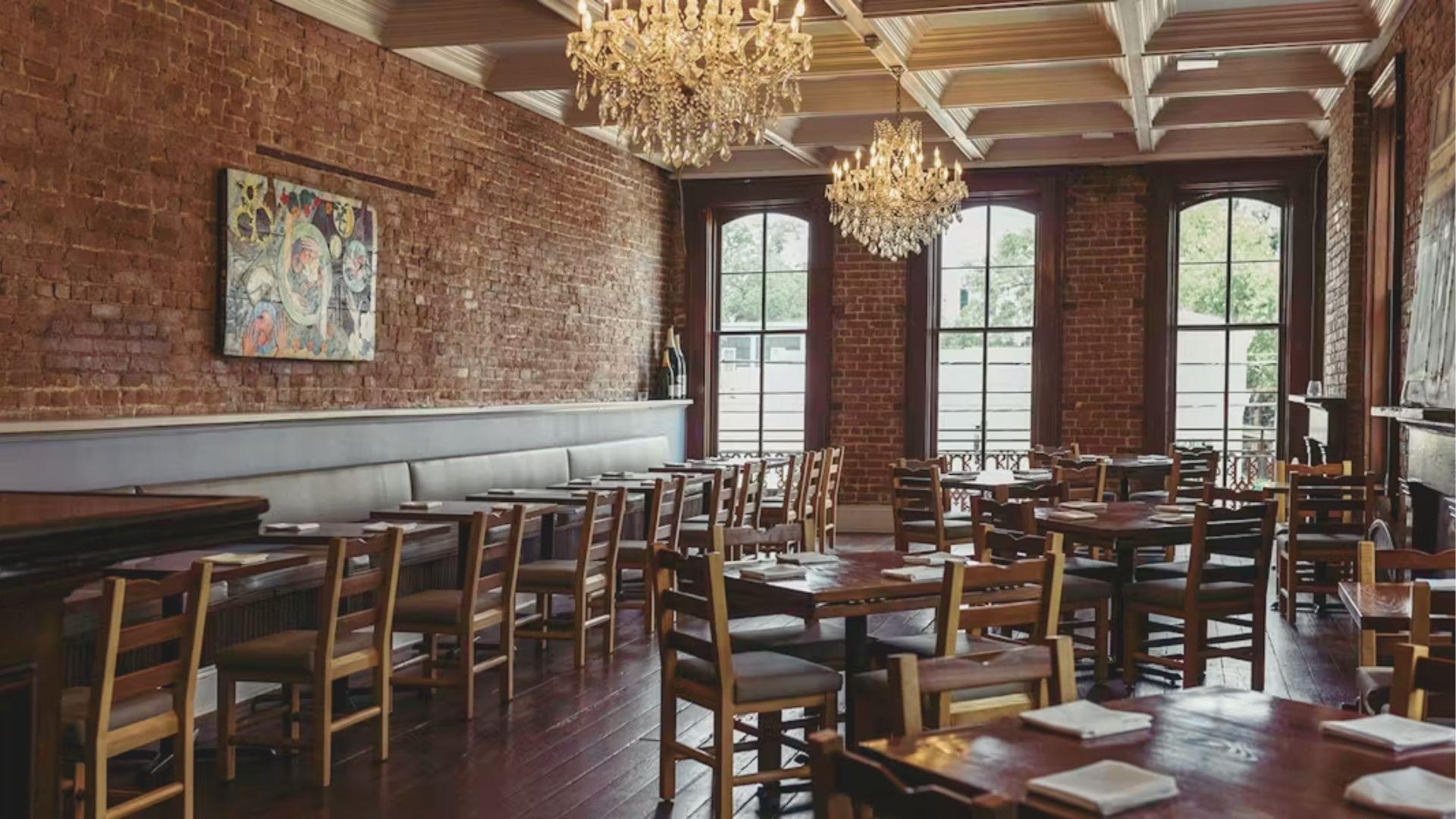 Classy dining room with exposed brick walls, dark wood tables, and crystal chandeliers at a top New Orleans restaurant.