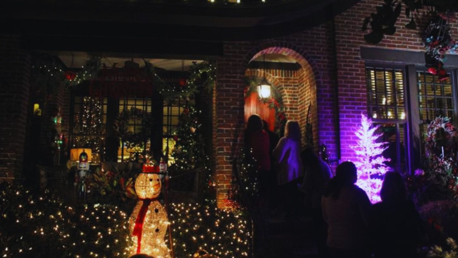 Visitors gather outside a decorated home during Augusta Christmas Tour of Homes with glowing holiday lights.