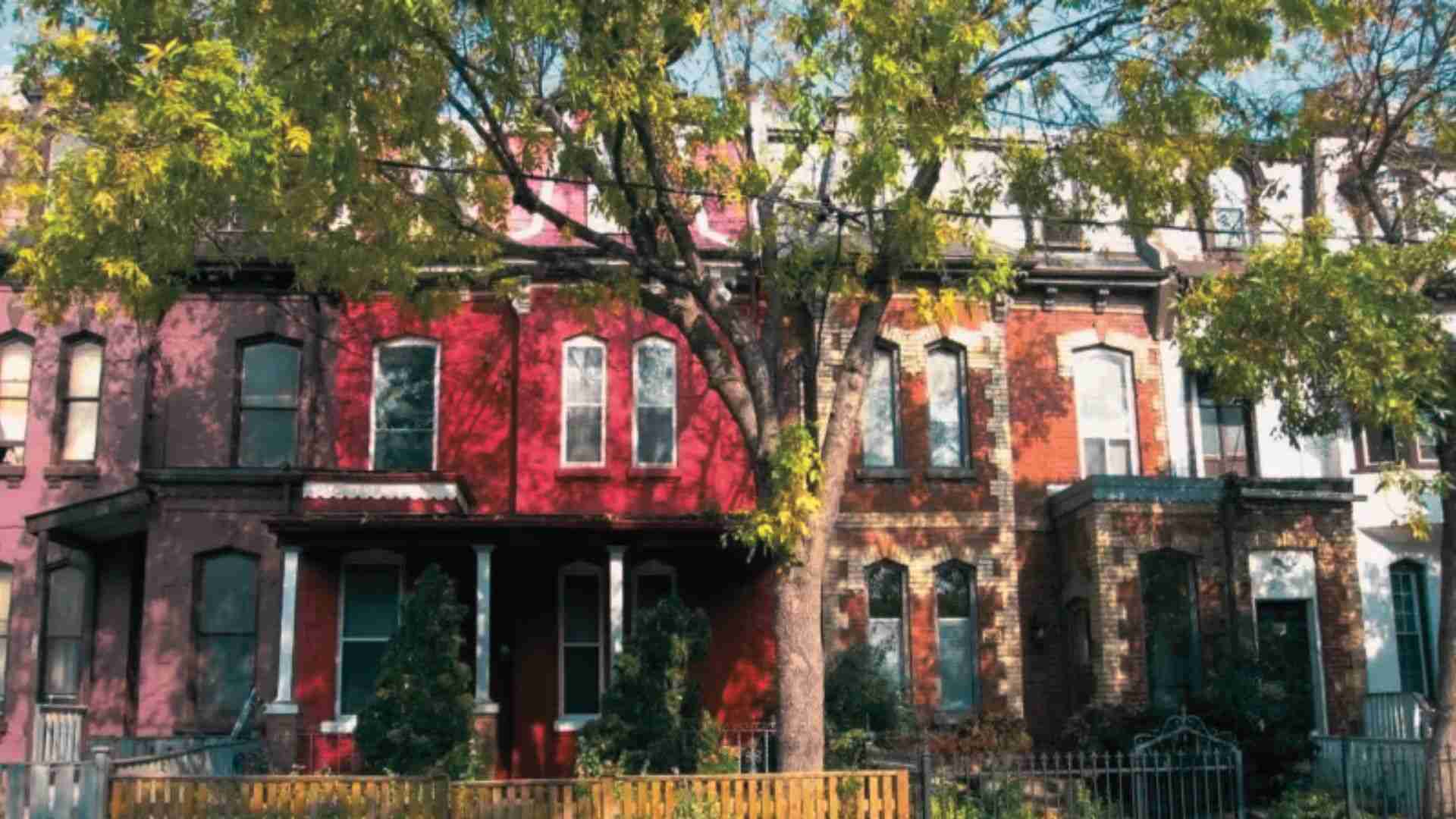 Colorful historic row houses beneath leafy trees in Atlanta's Cabbagetown neighborhood on a sunny day.