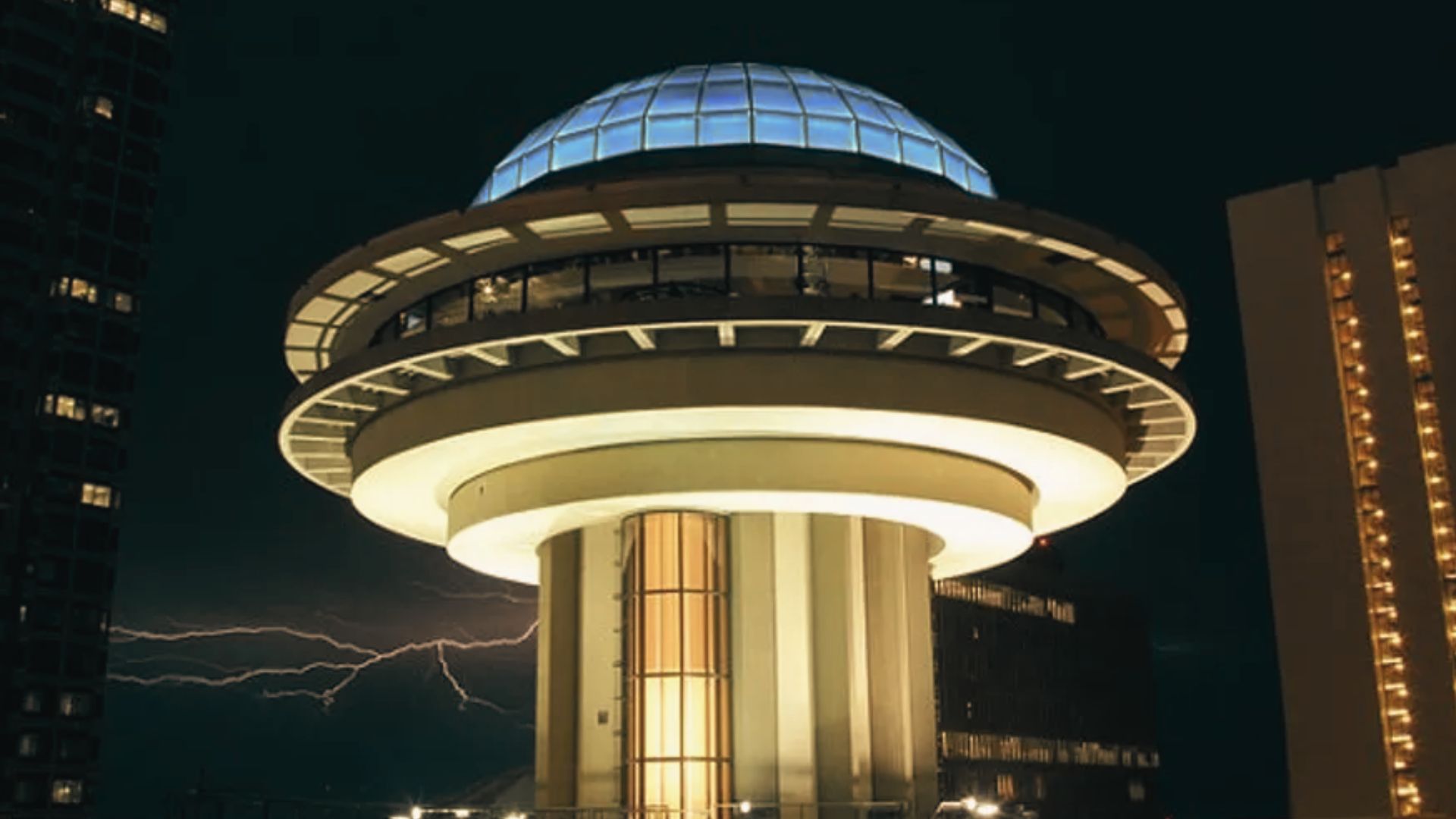 Night view of Atlanta's Polaris building glowing beneath dark skies with lightning near surrounding towers.