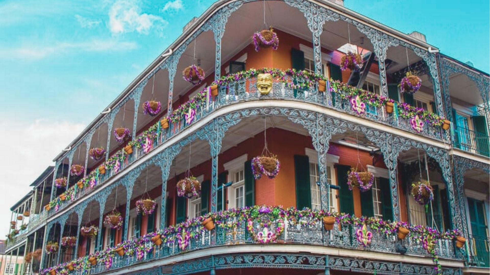 Colorful French Quarter building with intricate cast-iron balconies draped in purple Mardi Gras flower baskets.