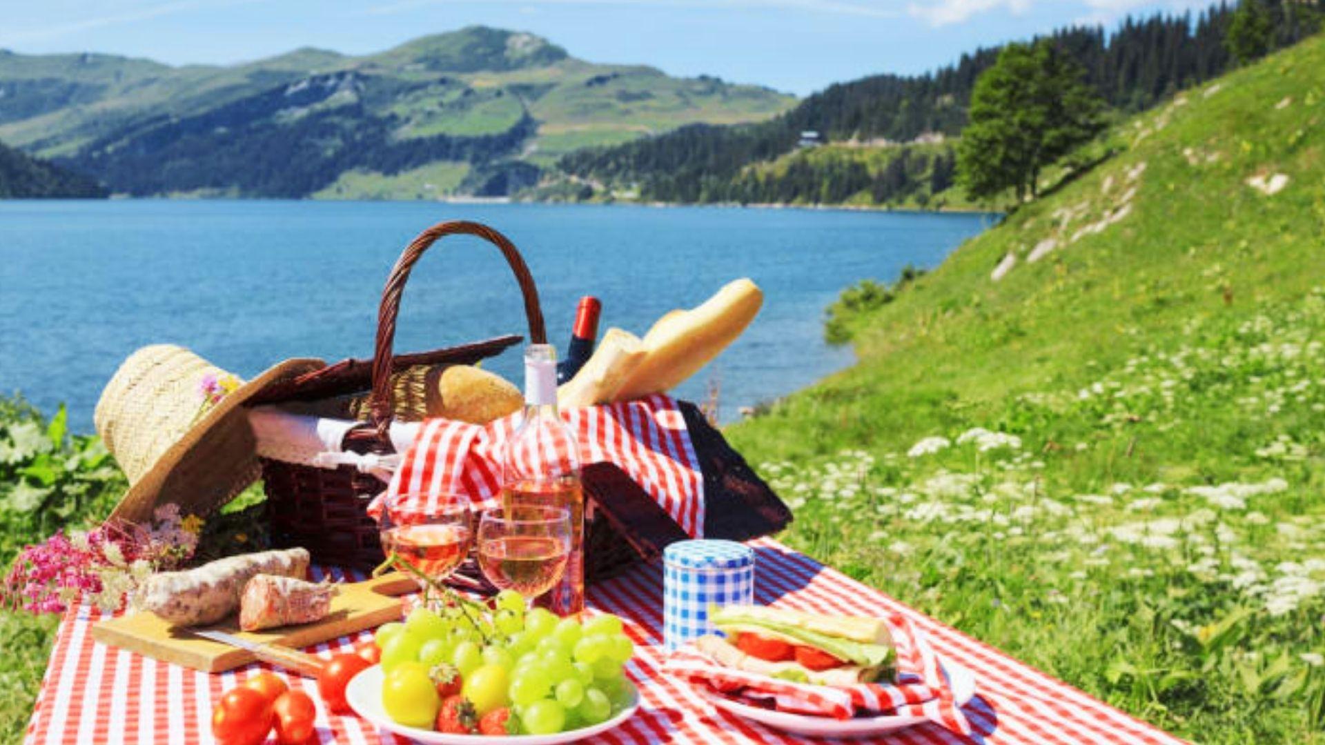 Lakeside picnic setup with food and wine near green hills