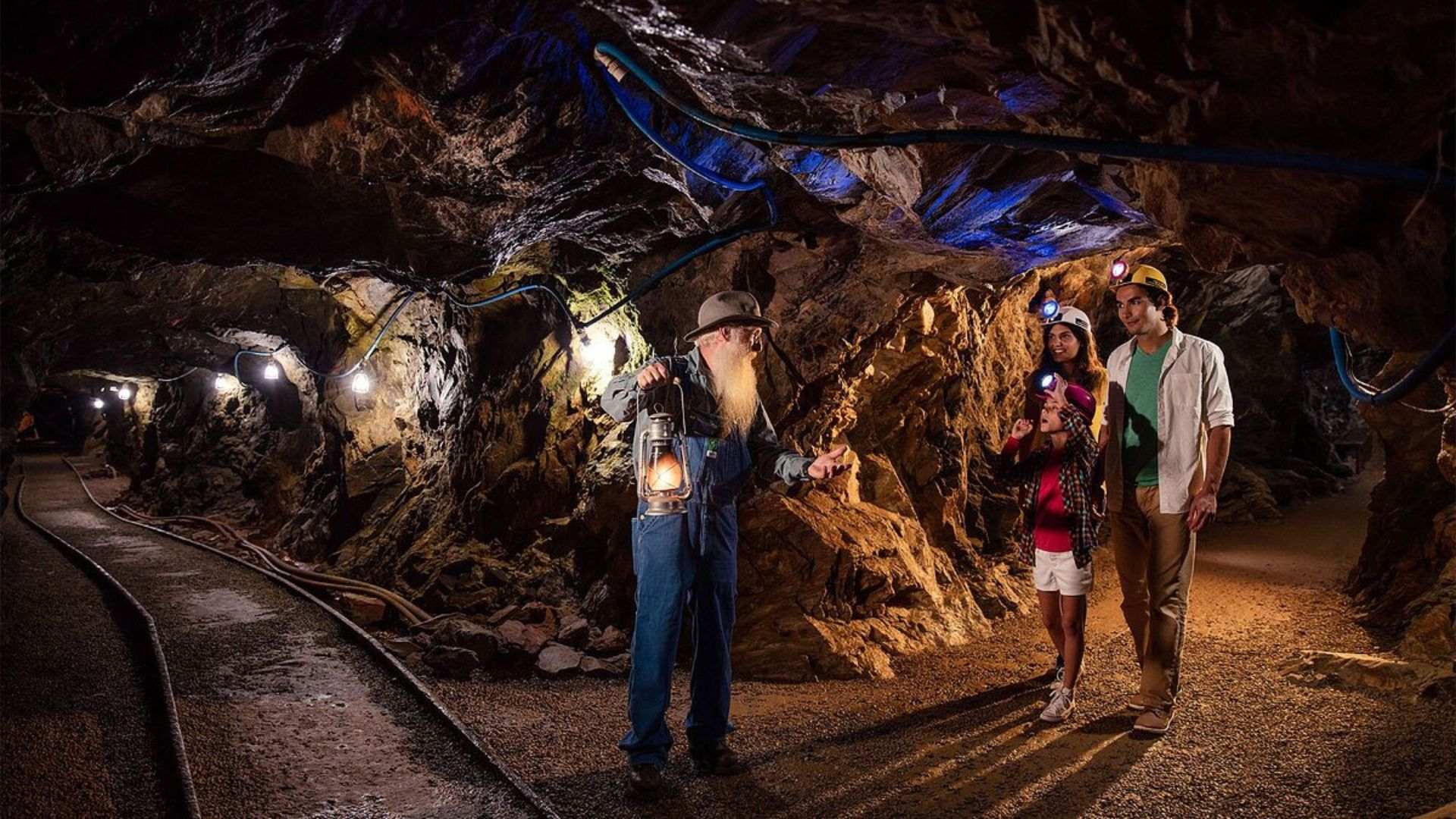 Visitors in a cave at Consolidated Gold Mine, surrounded by rock formations, with a light source highlighting their exploration.
