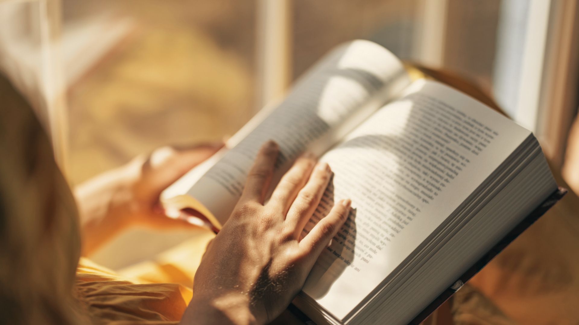 Person reading an open book in sunlight, showing how reading improves focus and calms the mind.