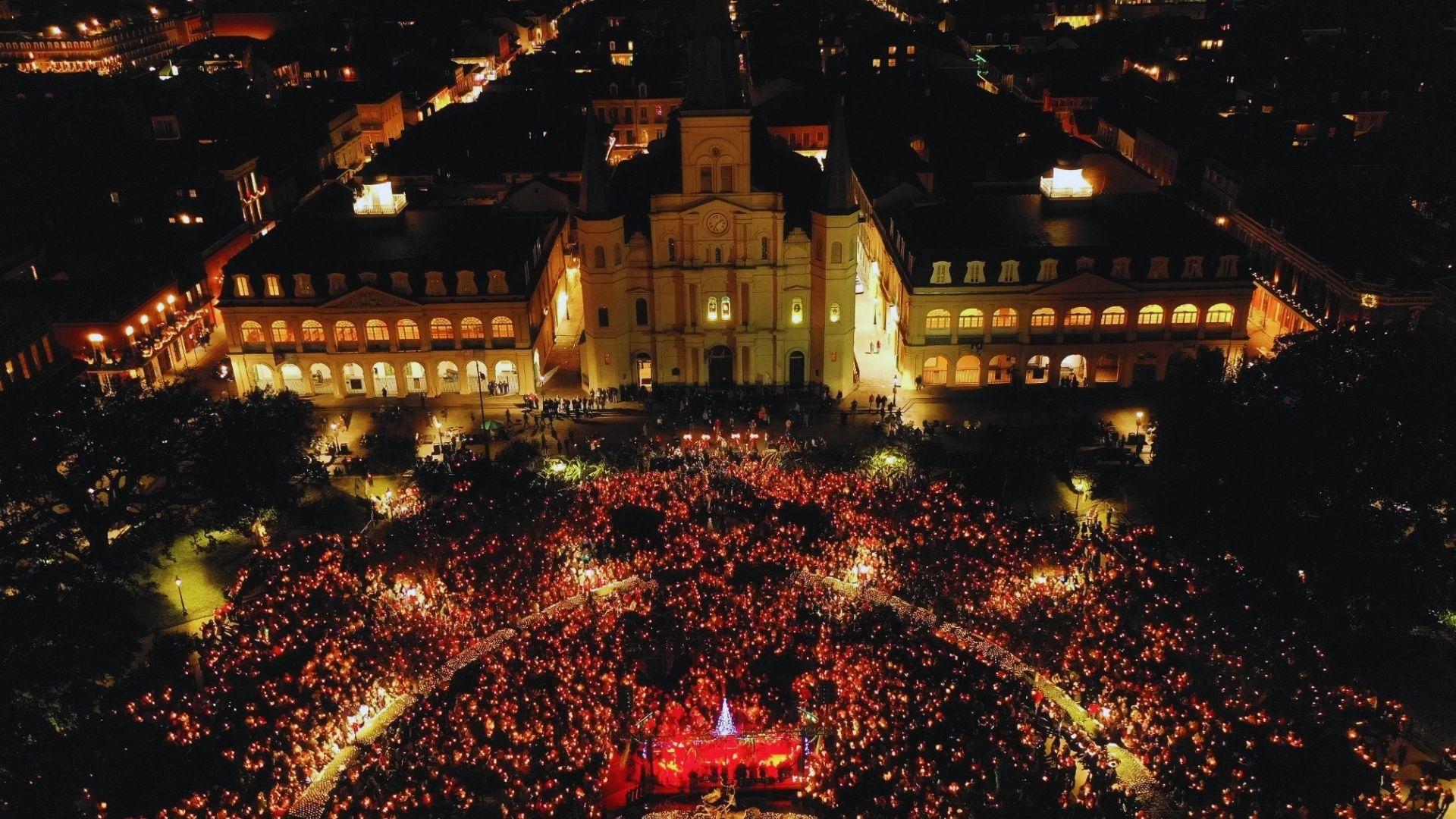 Aerial view of Jackson Square at night filled with thousands holding candles, St. Louis Cathedral lit, stage glowing