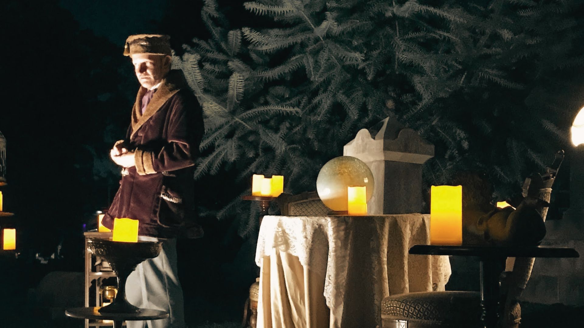 Candlelit historical reenactment scene at Oakland Cemetery featuring a person in vintage attire beside a display table.