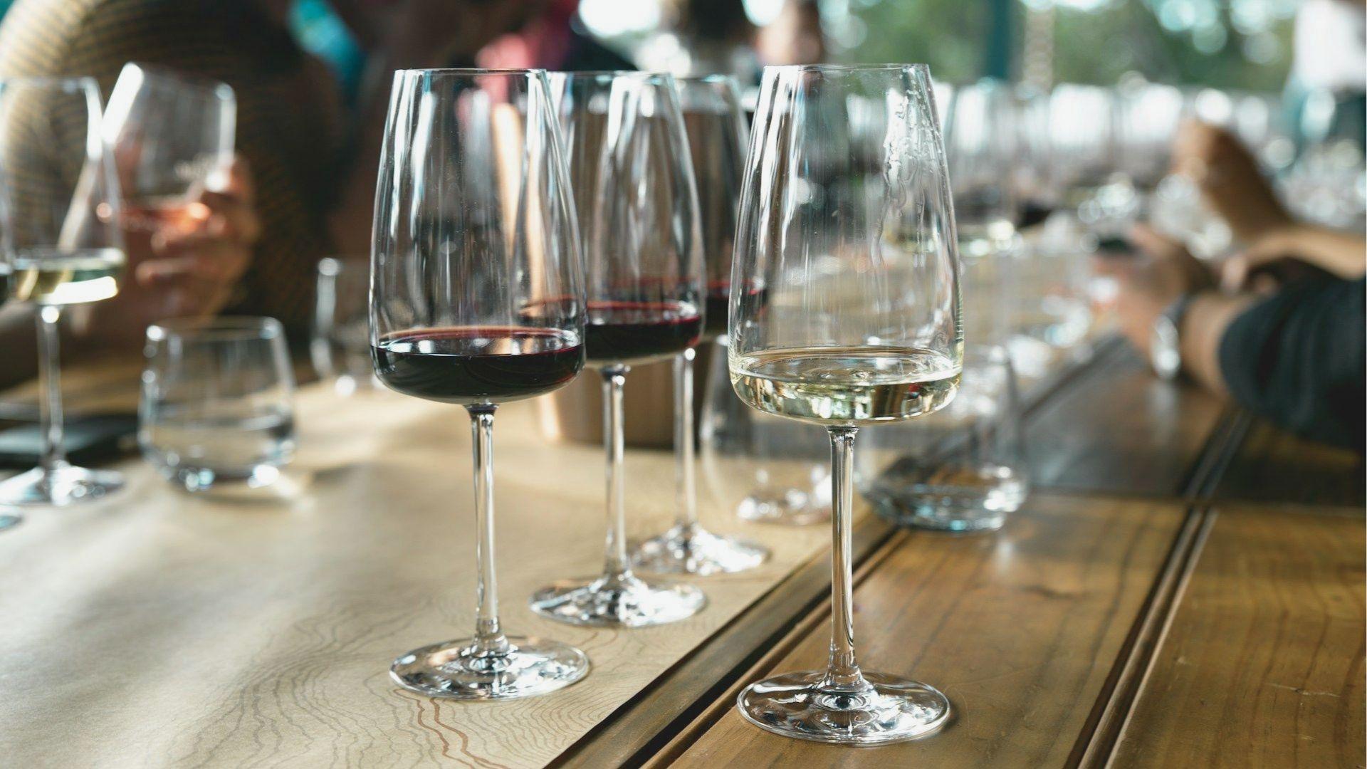 Glasses of red and white wine are lined up on a wooden tasting bar for a flight at a local winery.