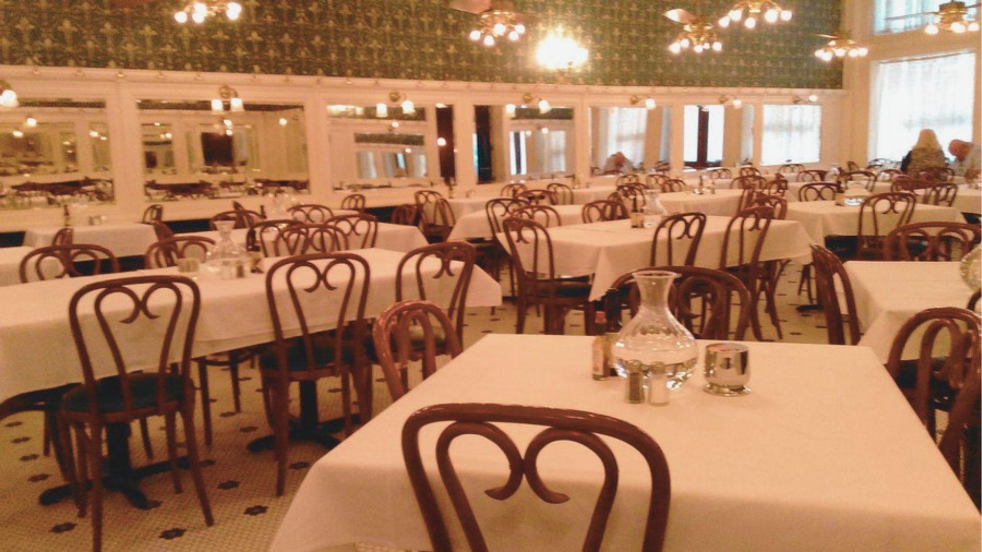 Warmly lit traditional dining room with mirrored walls, green fleur-de-lis wallpaper, and bentwood chairs.