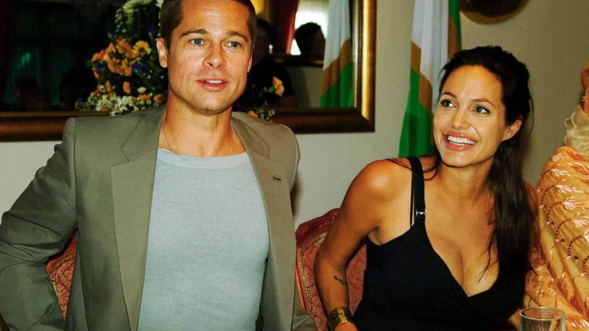 Brad Pitt in gray blazer and Angelina Jolie in black dress smiling together at formal event