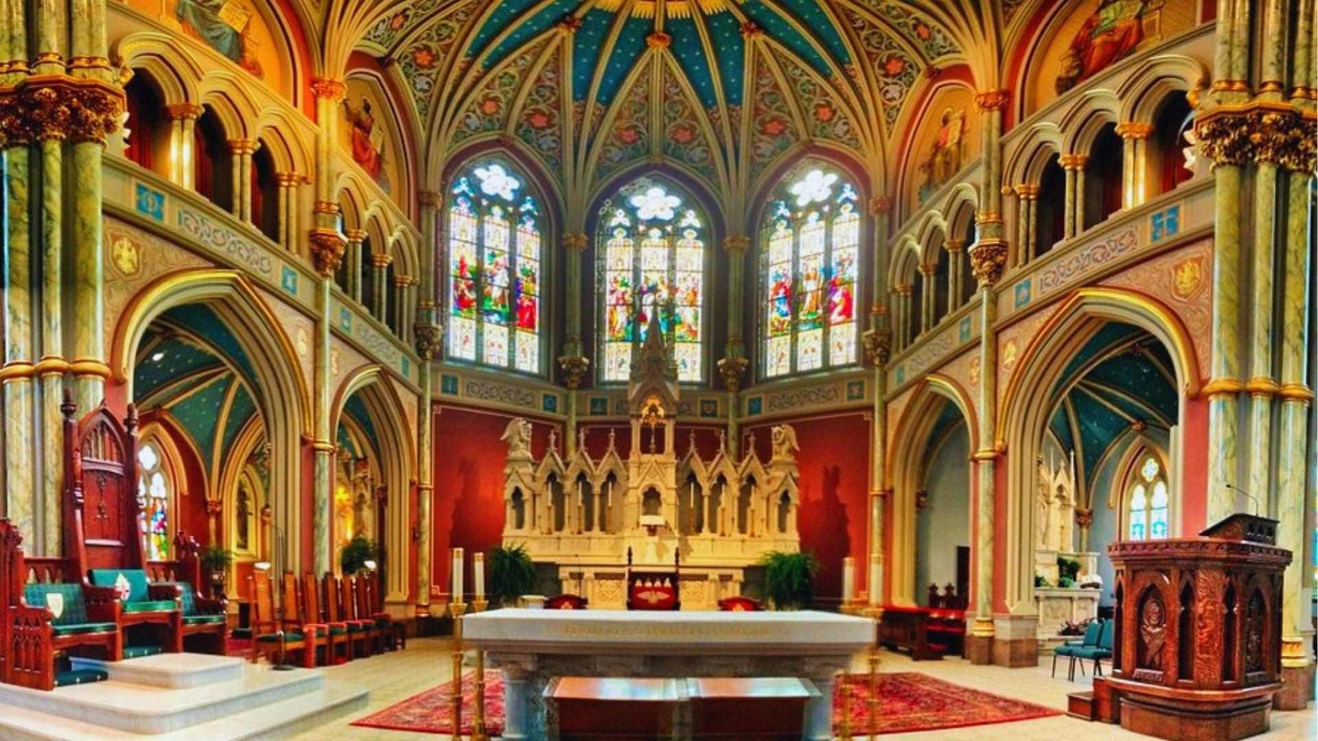 Ornate interior of Cathedral Basilica of St. John the Baptist with stained glass and gold details.