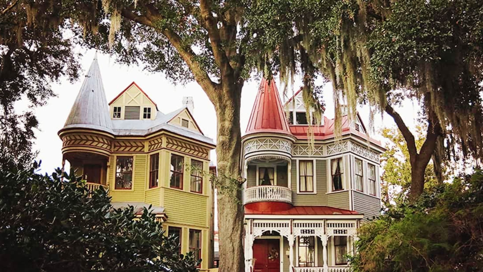 Two Victorian homes with turrets and gingerbread trim behind Spanish moss-covered oaks