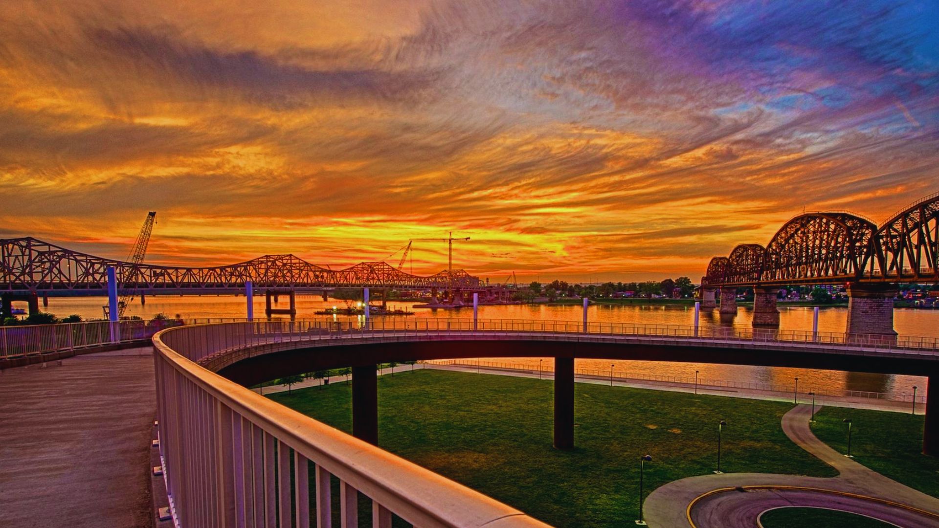 Curving riverside walkway overlooks glowing sunset skies and historic bridges.
