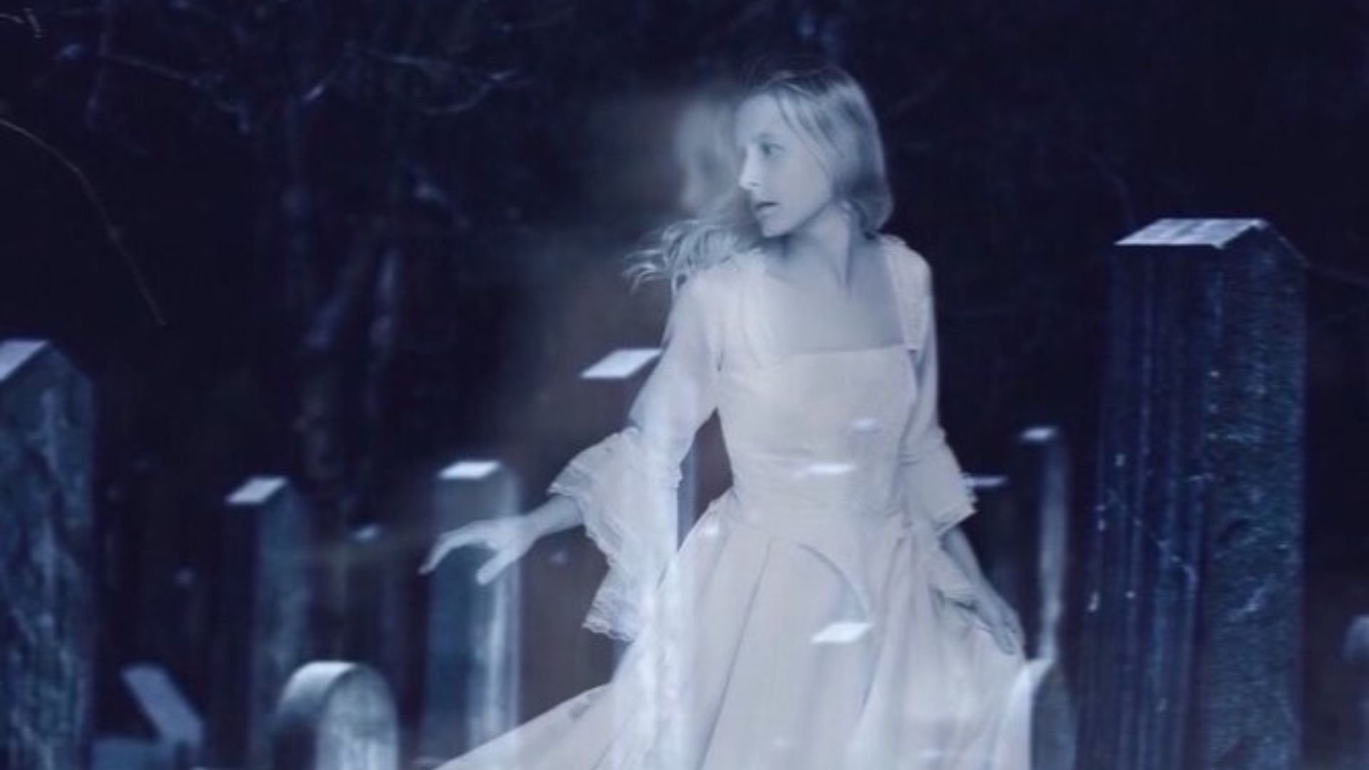 Translucent ghostly woman in white vintage dress walking through a dark cemetery among old gravestones.