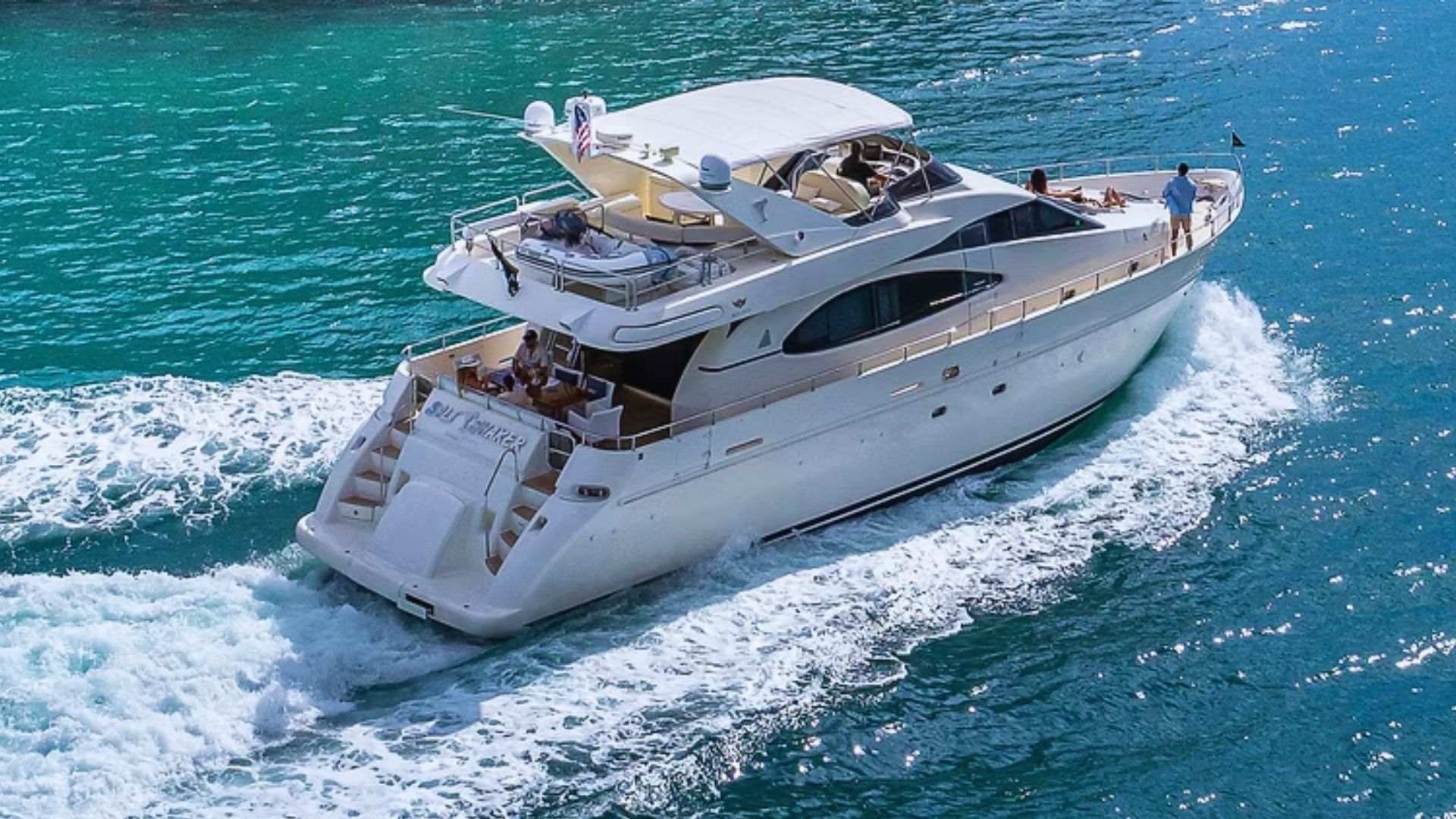 A white yacht cruises across turquoise water with people relaxing on board.