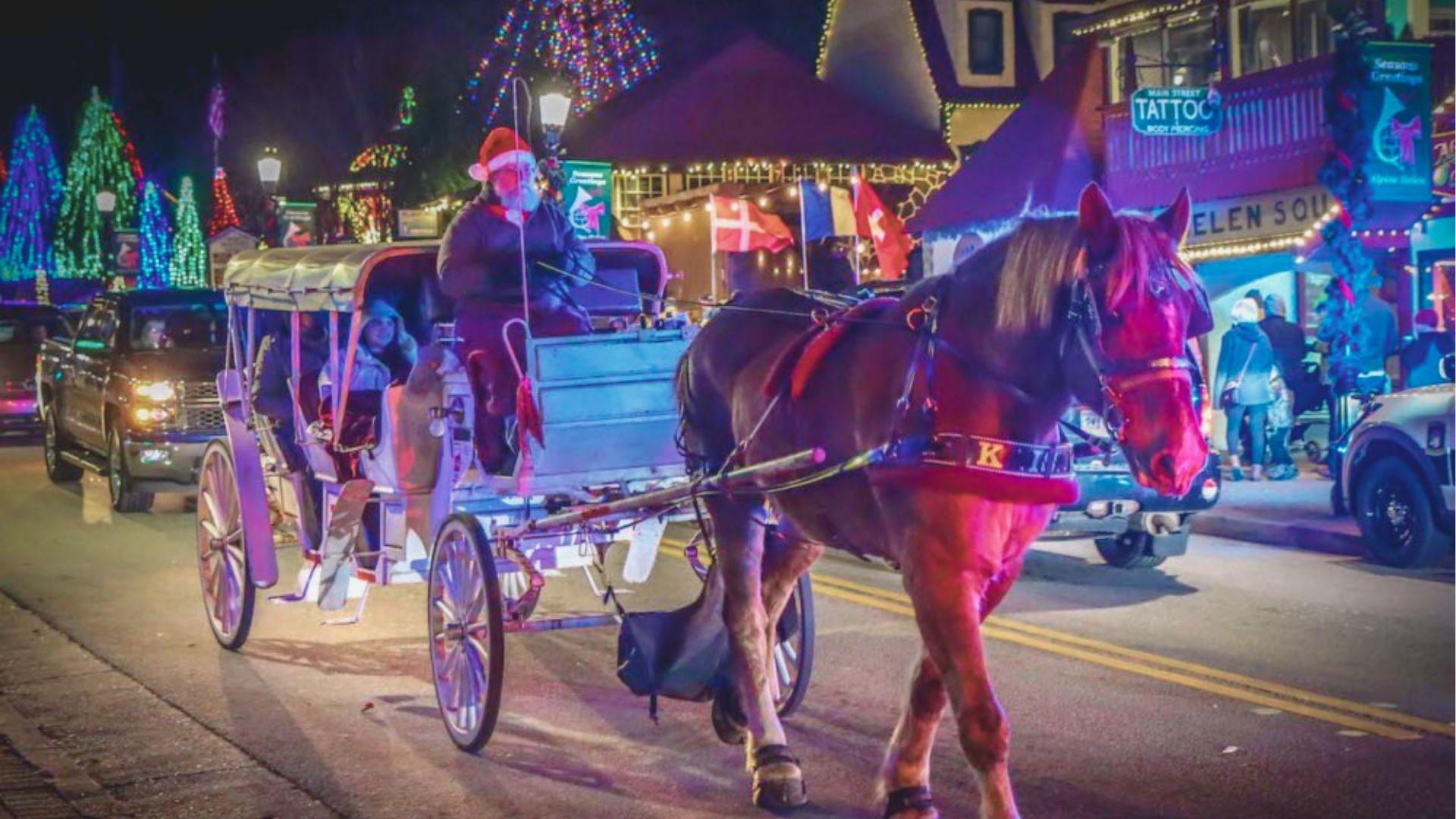 Horse-drawn carriage driven by a Santa-hatted driver carries passengers down Helen’s Main Street at night.