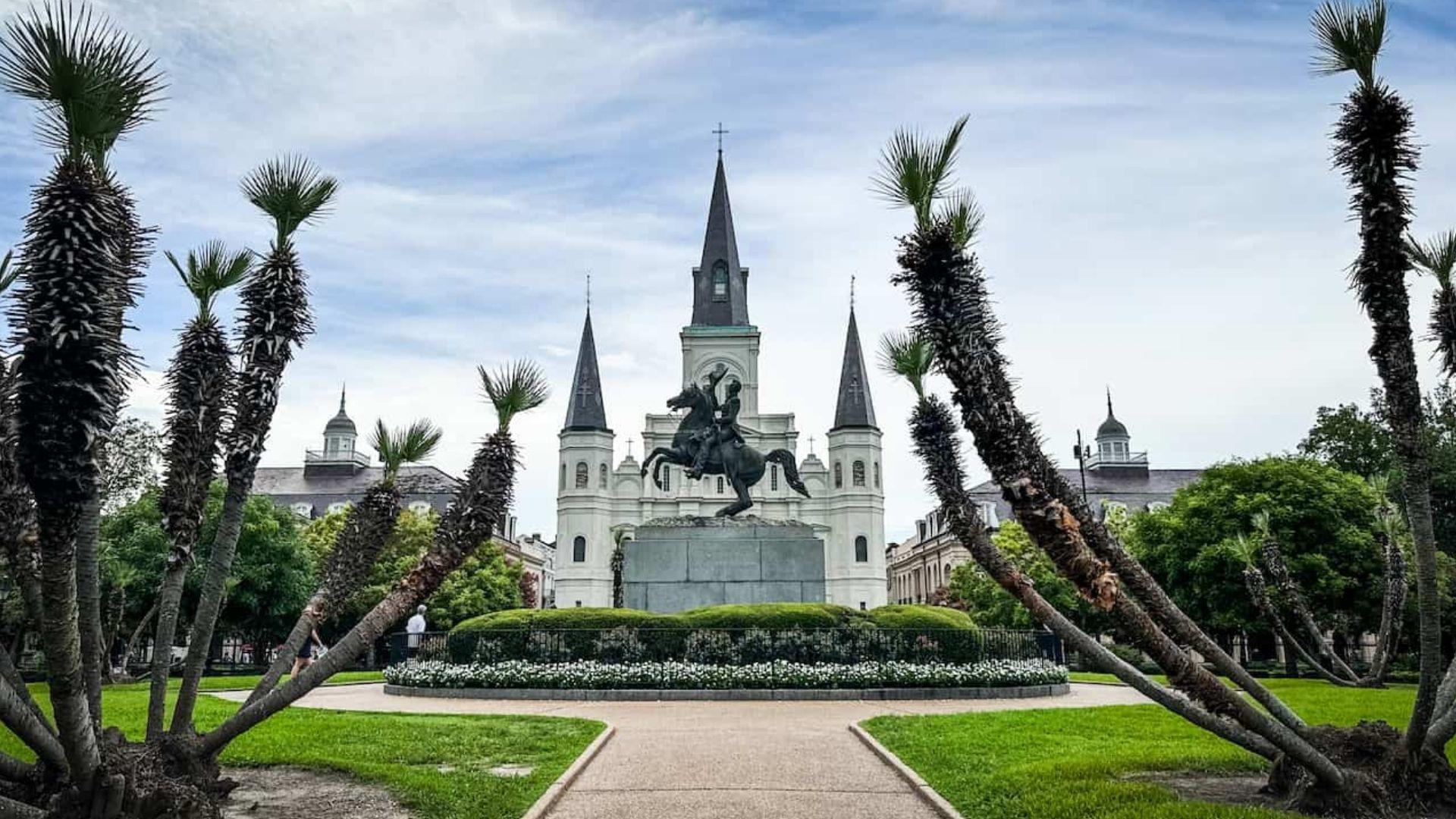 Andrew Jackson equestrian statue in Jackson Square framed by palm trees, with St. Louis Cathedral spires, green lawns, New Orleans