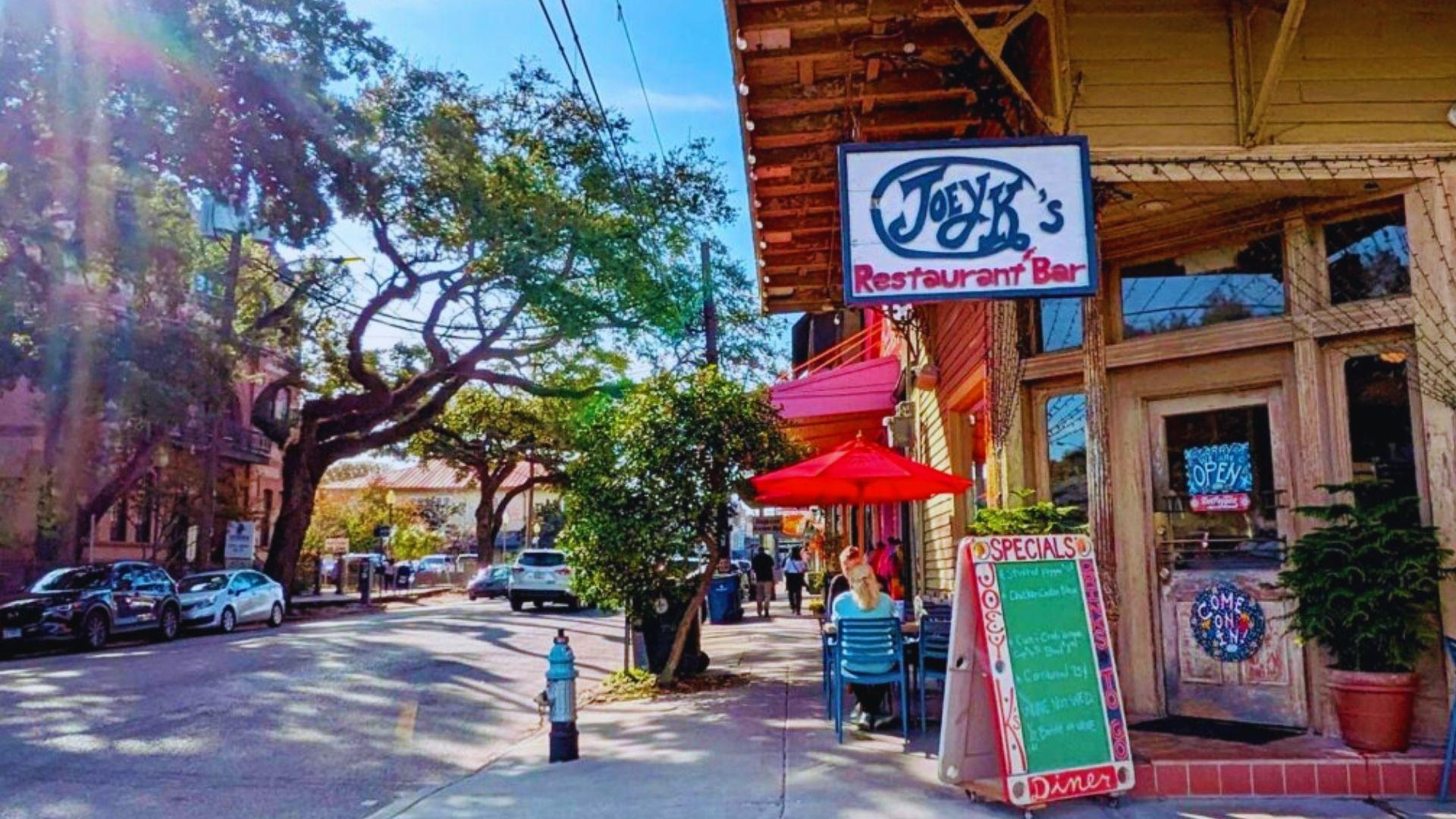 Joey K’s Restaurant Bar on sunny Magazine Street corner with red umbrella, specials chalkboard, blue fire hydrant, oaks