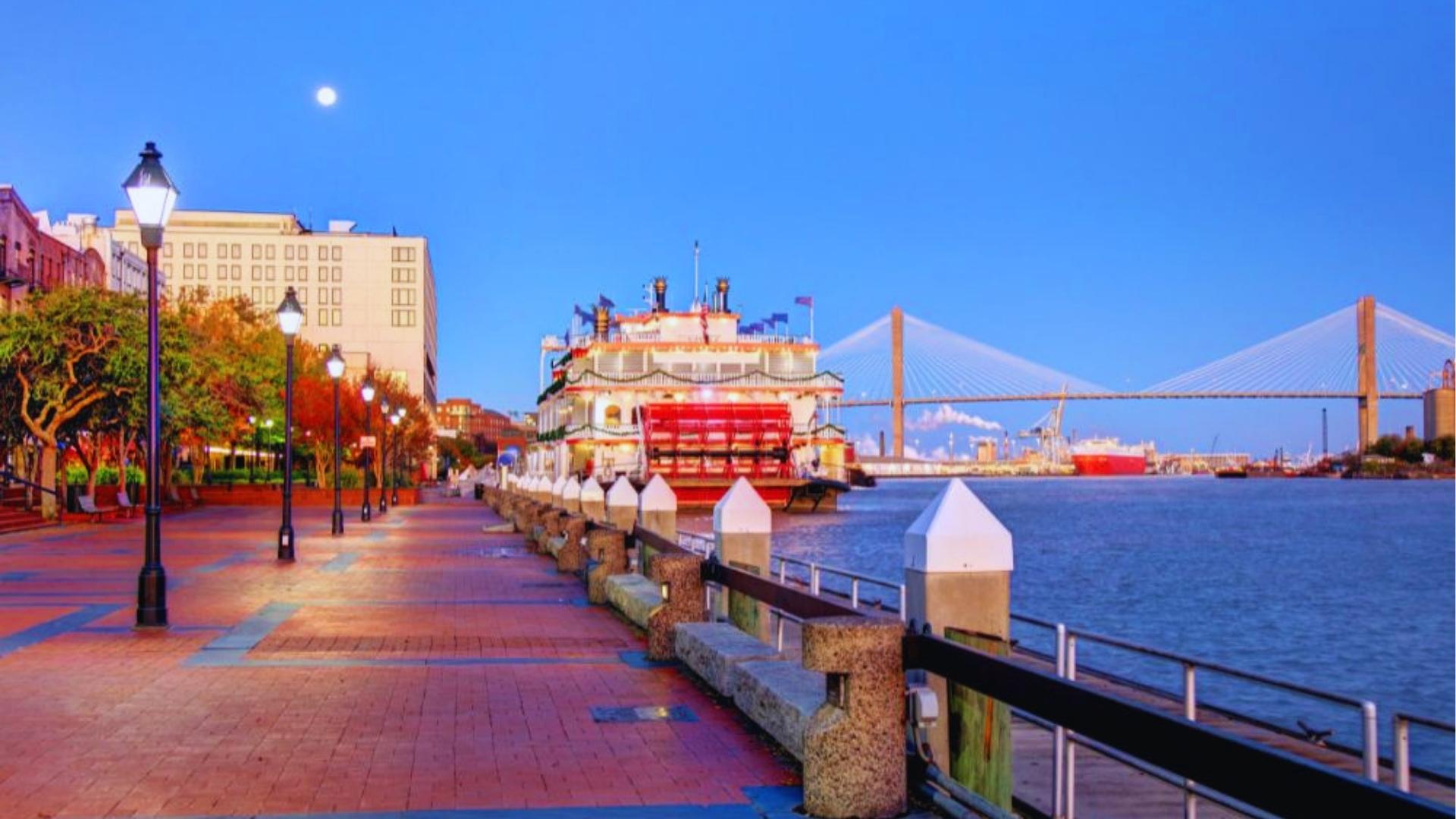 Savannah Riverfront at twilight with Georgia Queen riverboat and Talmadge Bridge lit up.