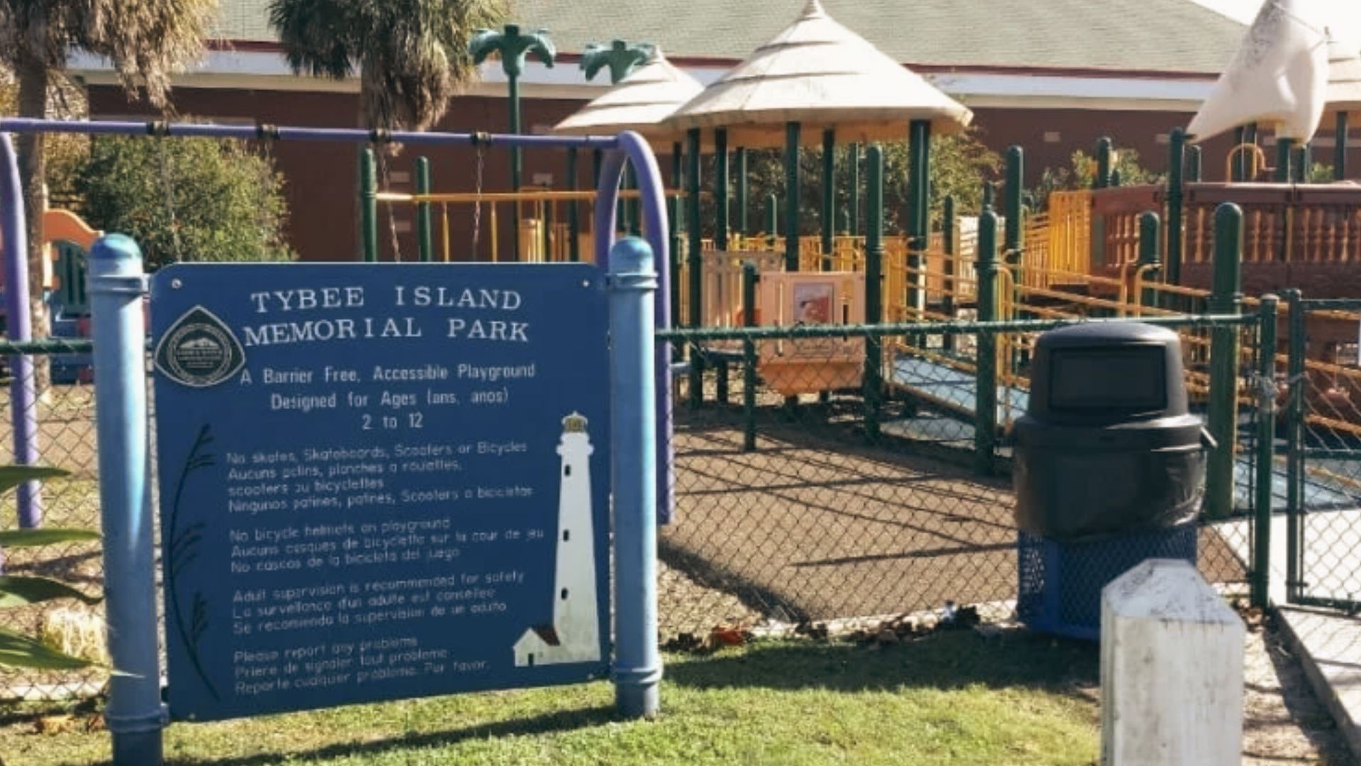 Sign for Tybee Island Memorial Park stands beside a fenced playground with play equipment nearby.