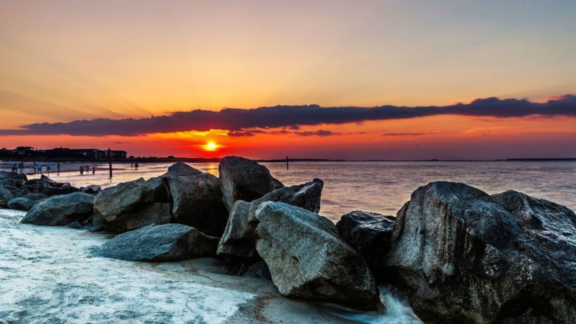 Large rocks sit beside calm water as the sun sets over the Tybee Island shoreline.