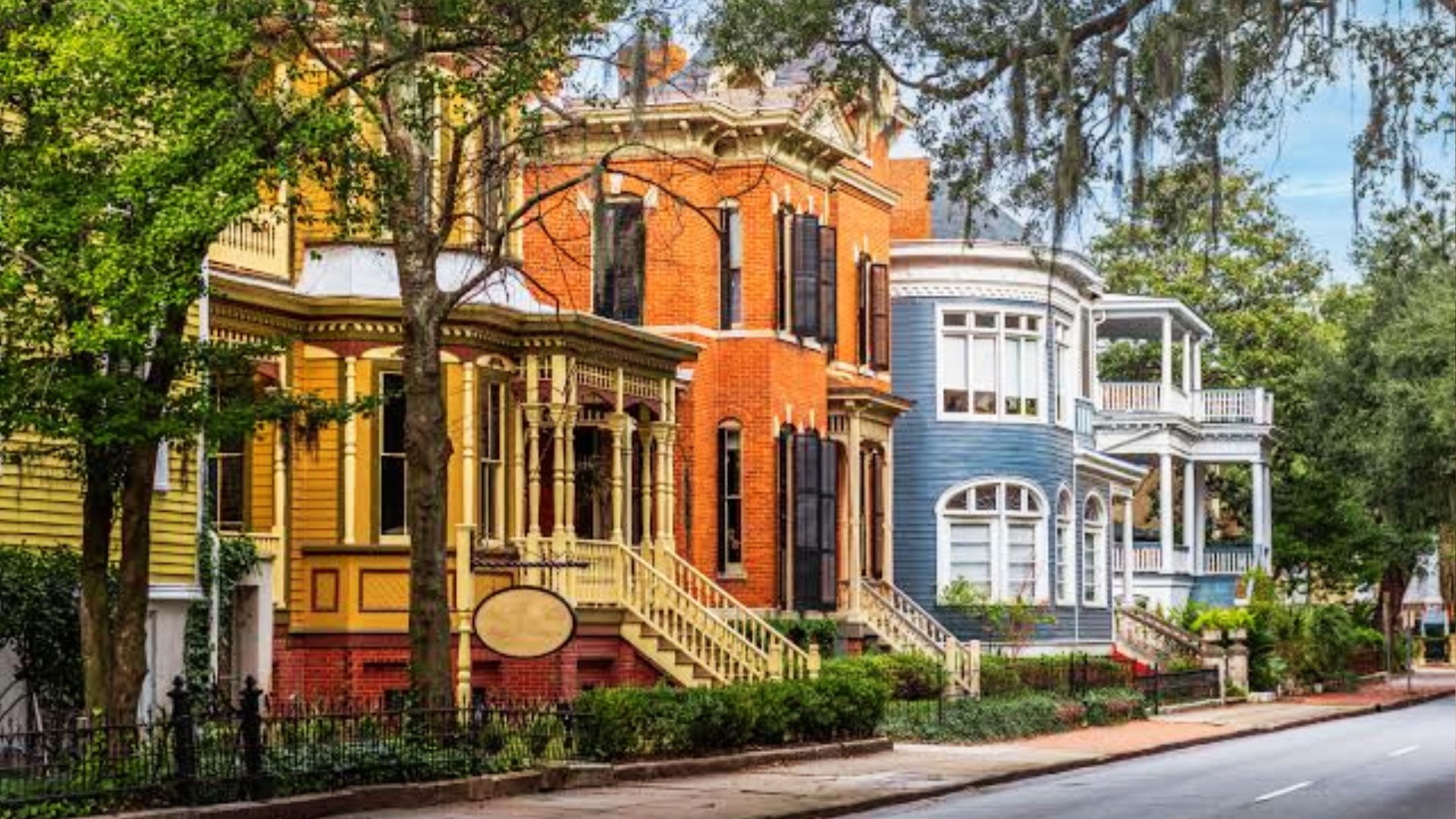 Row of colorful Victorian homes in yellow, red brick, and blue with Spanish moss trees