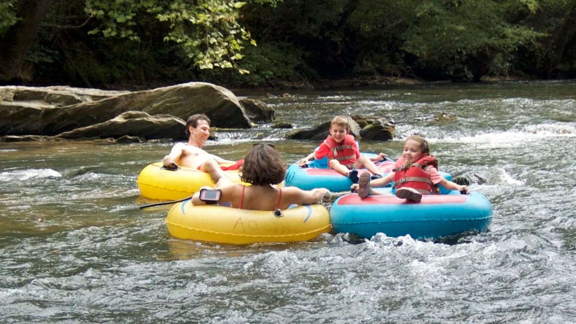 Four family members float on colorful tubes down a river in North Georgia, enjoying a sunny day amidst nature.