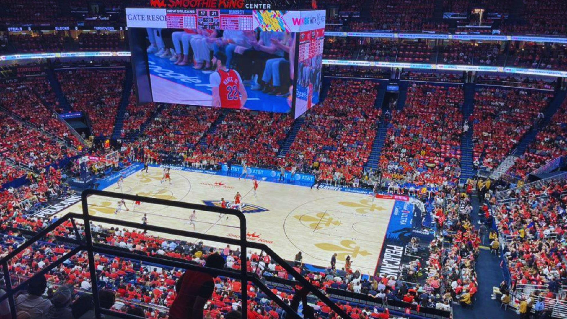 New Orleans Pelicans game at Smoothie King Center with sea of red shirts, jumbotron, court action, packed arena