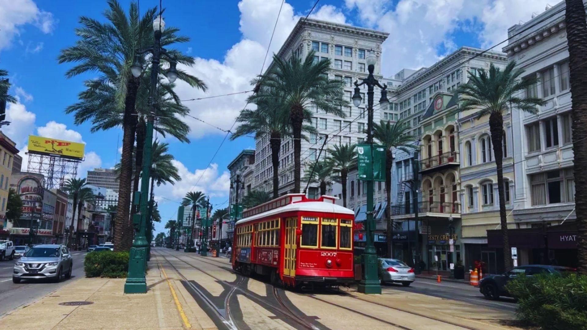 Red Canal Street streetcar 2007 travels along palm-lined tracks past historic buildings, blue sky, cars, New Orleans
