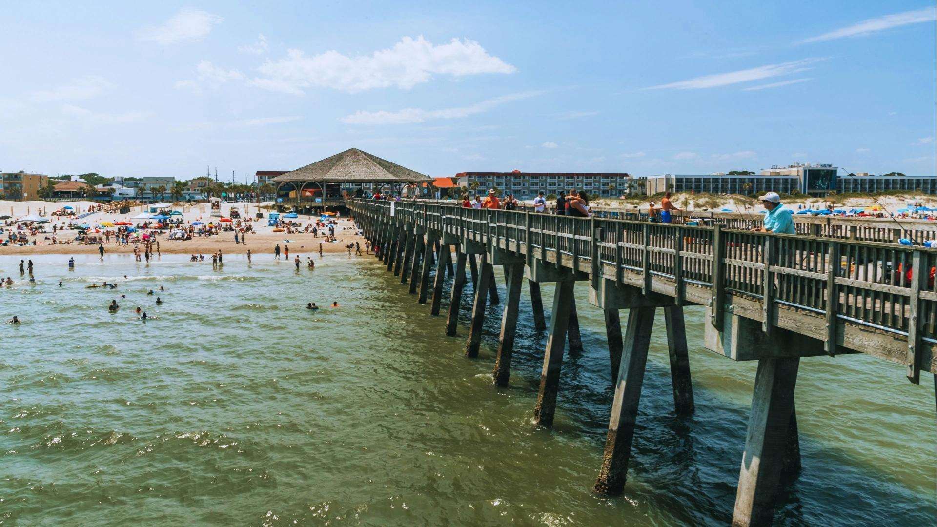 Crowded Tybee Island Pier with beachgoers swimming and fishing on a sunny day near Savannah.
