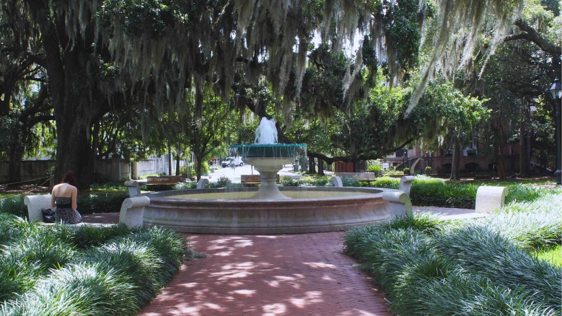 Lafayette Square fountain under moss-draped oaks with a woman relaxing on a bench in Savannah.
