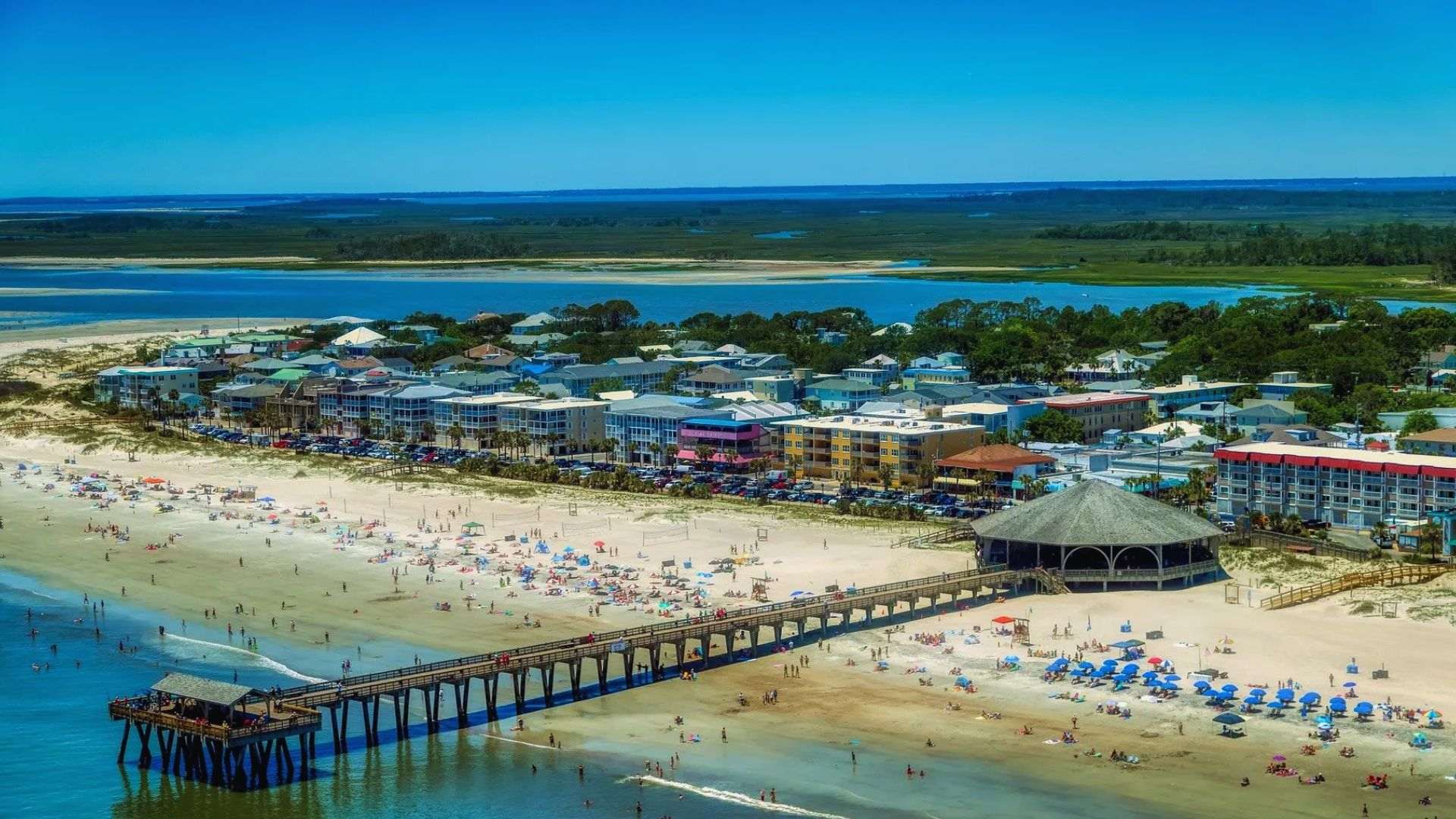 Aerial view of Tybee Island beach, long pier, blue water, sandy shore, hotels, visitors.