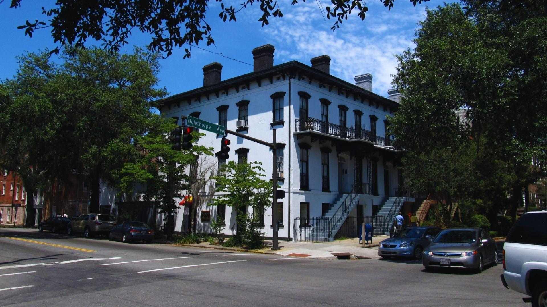 White historic corner building at Oglethorpe Avenue intersection with traffic lights and parked cars nearby.