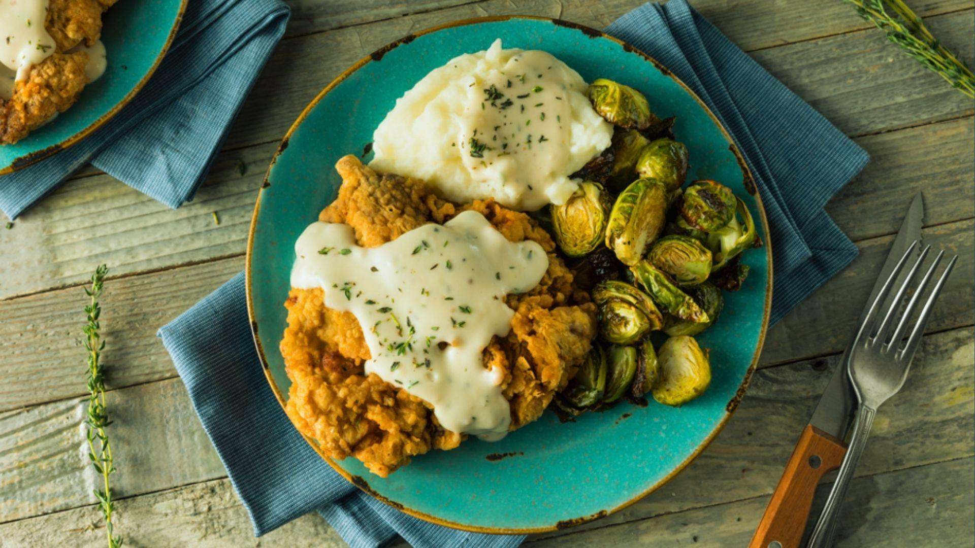 Crispy fried chicken with gravy, mashed potatoes and roasted Brussels sprouts on teal plate