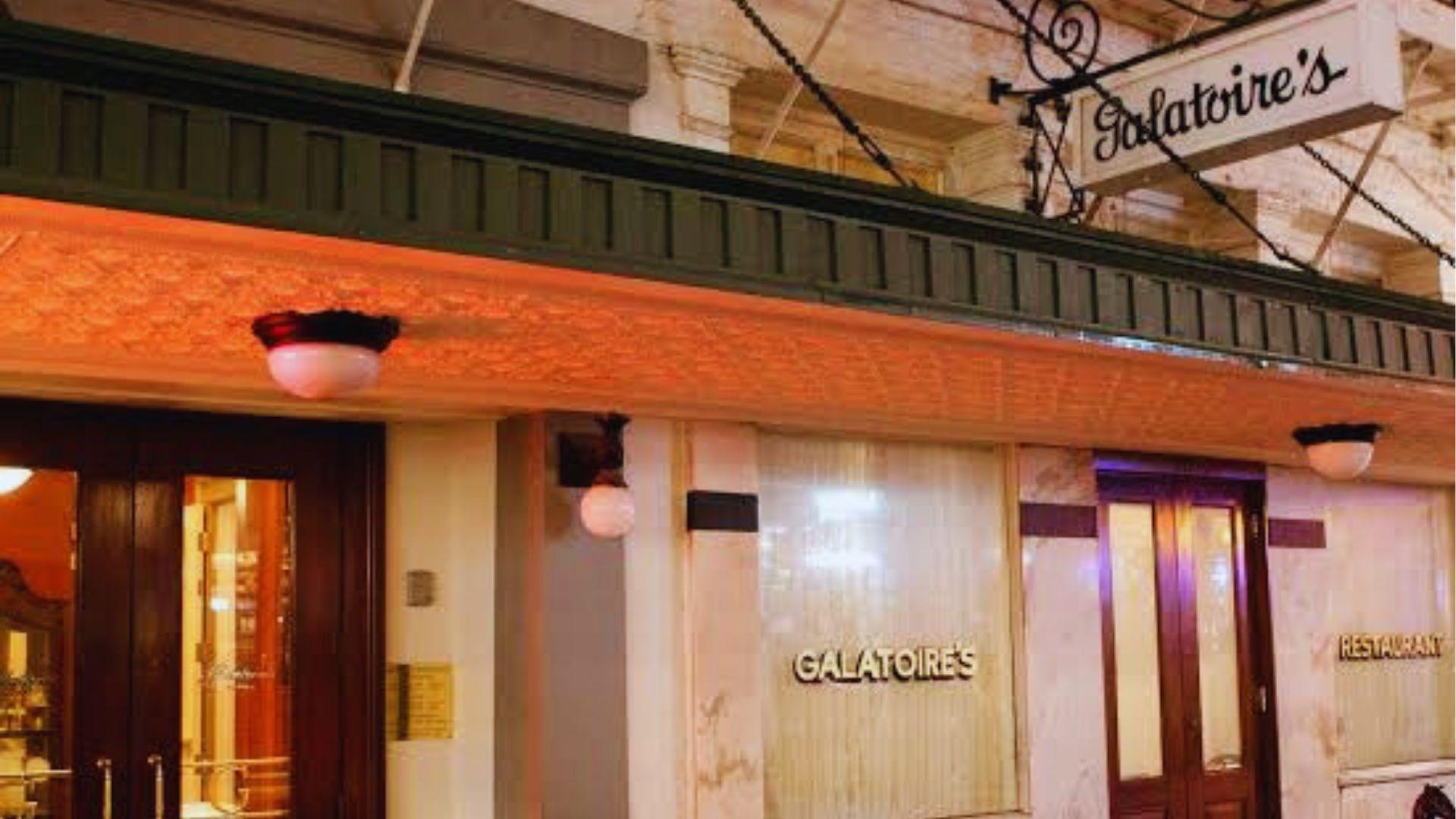 Galatoire's Restaurant at night with illuminated sign marble facade and wooden doors glowing warmly outside.