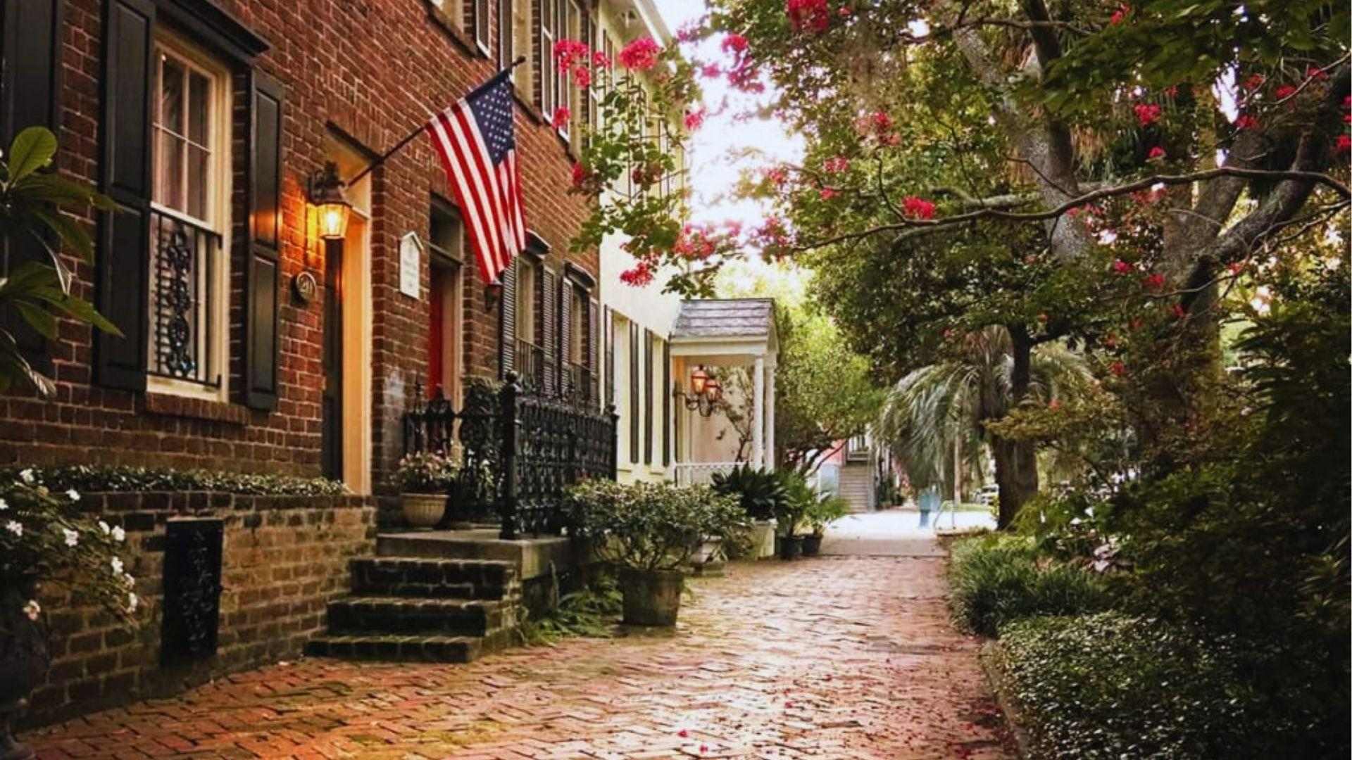 Brick sidewalk lined with historic brick homes, American flag glowing lanterns and blooming pink trees.
