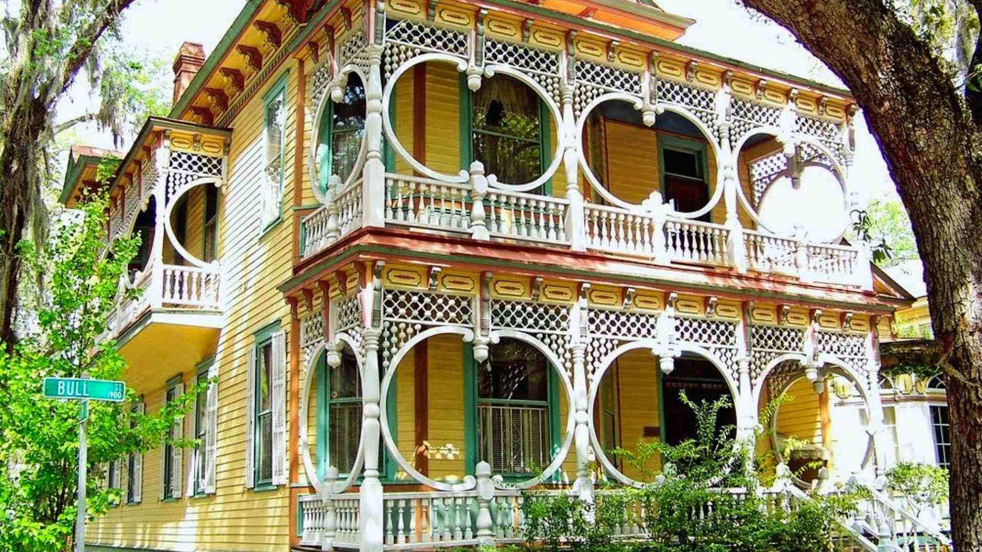 Yellow Victorian house with ornate white circular trim on double porches, Bull St corner