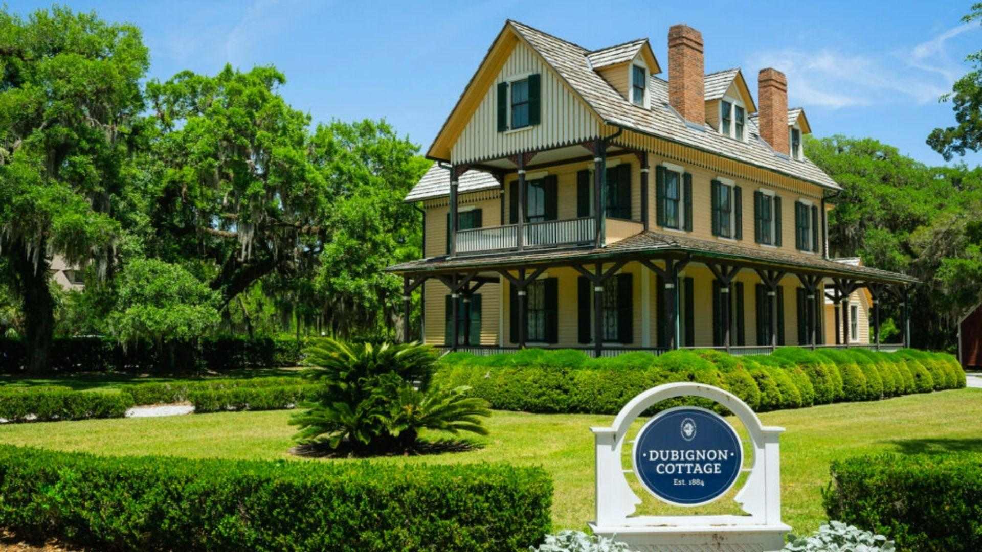 Two-story yellow Victorian house with green shutters, porch, and Dubignon Cottage 1884 sign in front