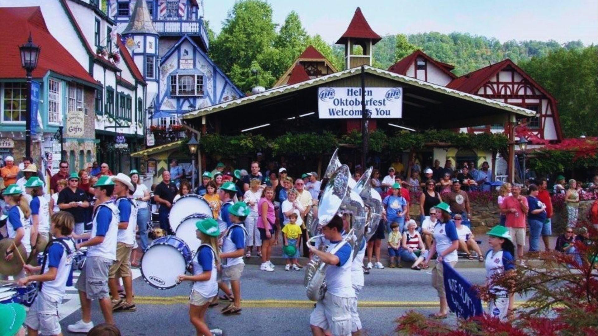 Marching band in hats playing drums and tubas parading through Helen Oktoberfest street with spectators.