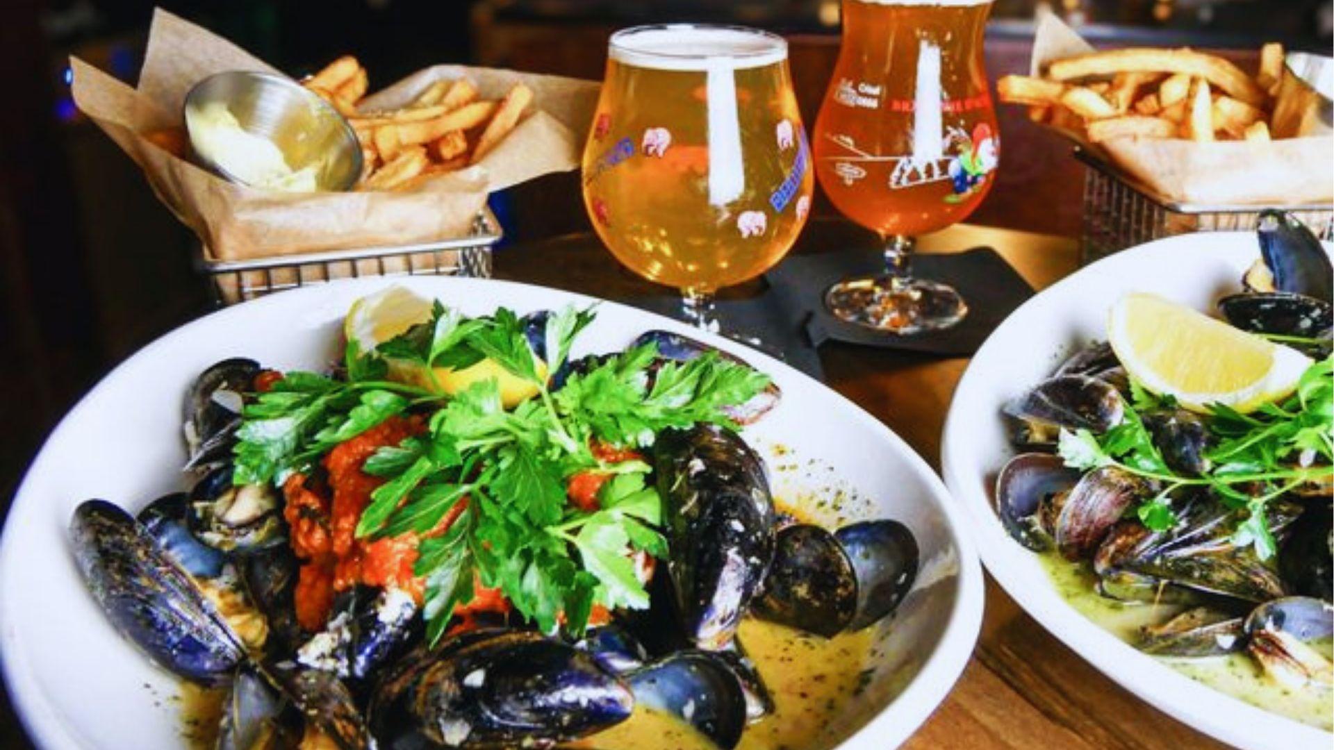 Bowls of steamed mussels garnished with parsley lemon served with french fries and craft beers.