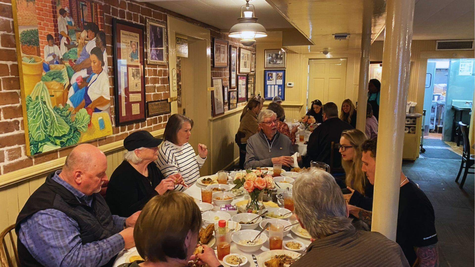 Group dining together at a long table enjoying southern comfort food with colorful wall art behind.