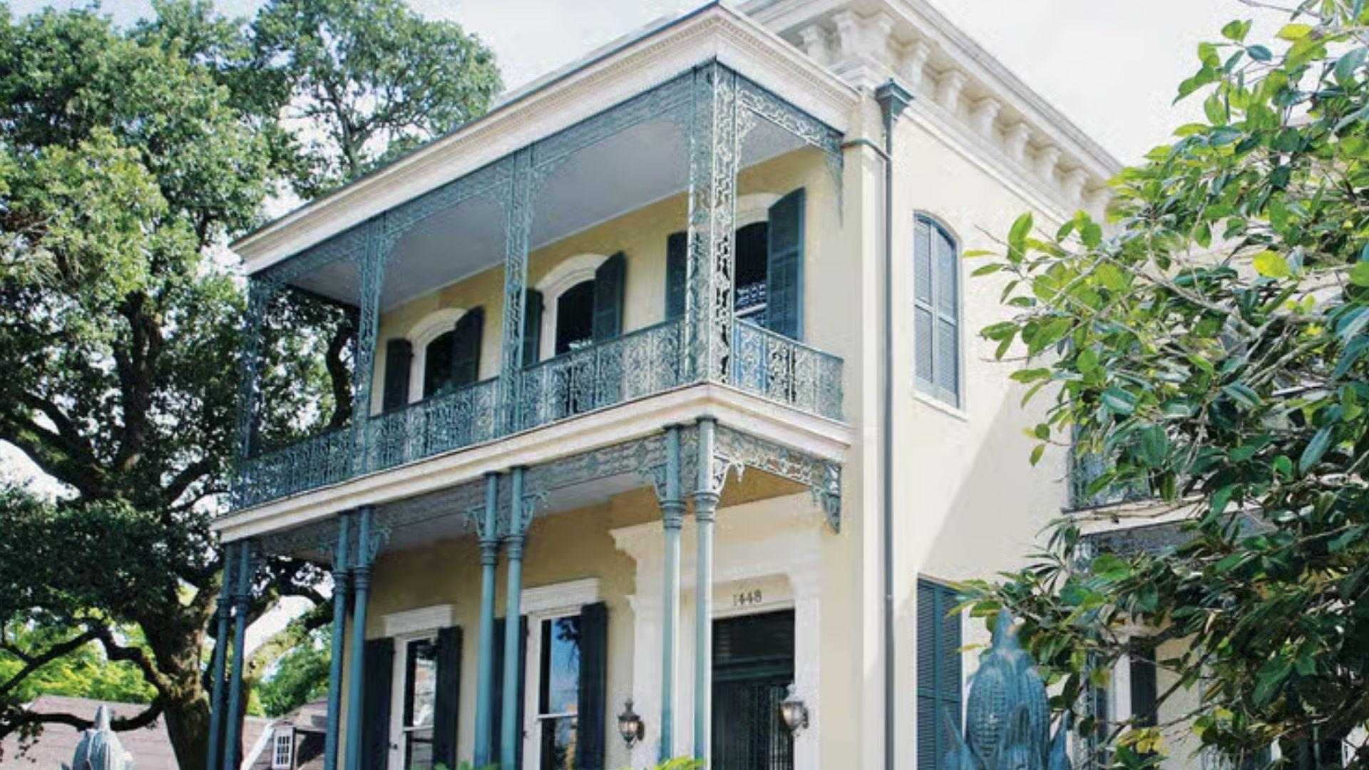 Historic yellow double-gallery mansion with ornate iron balconies behind cornstalk fence