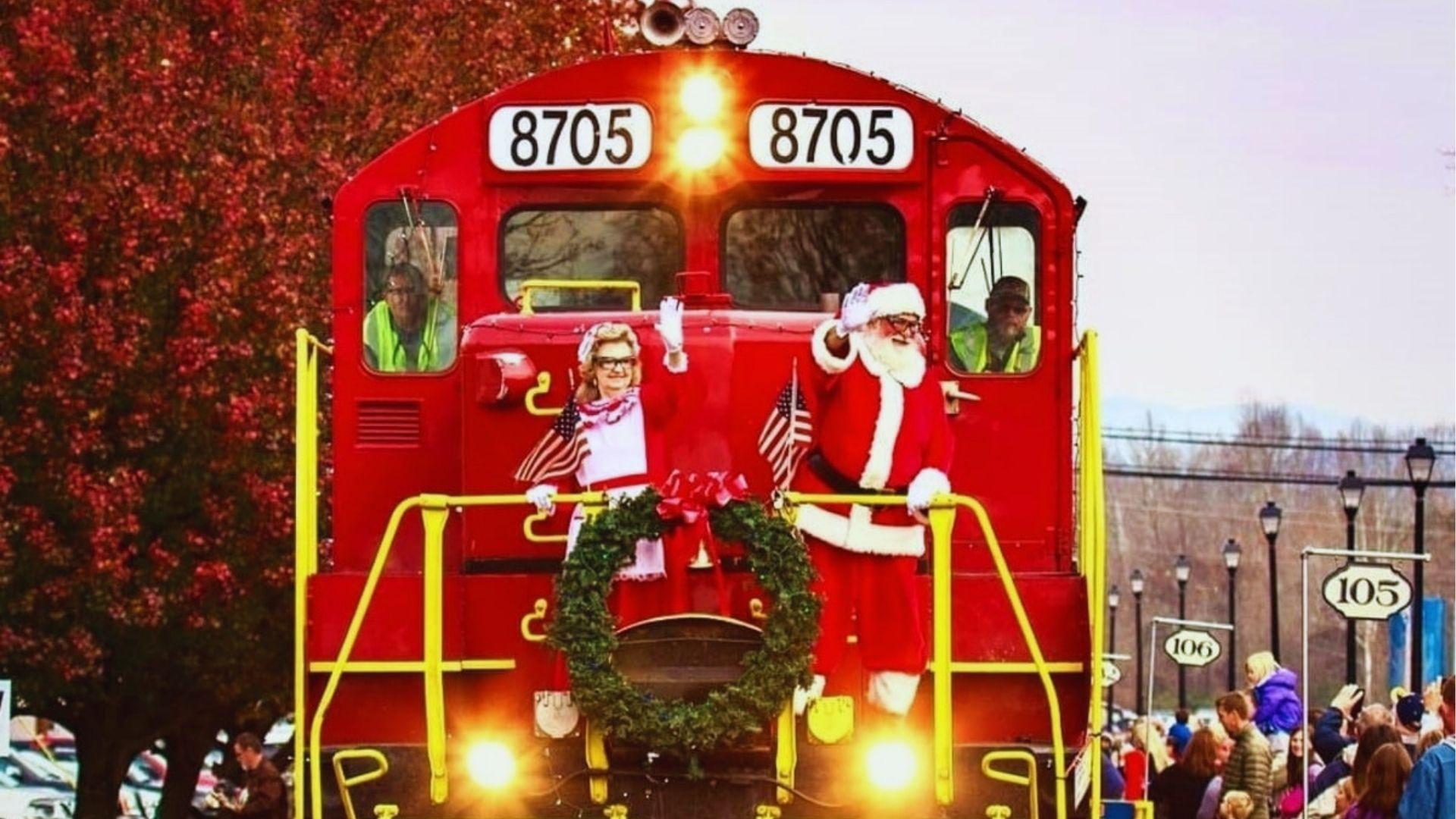 Santa and Mrs Claus waving from locomotive numbered 8705 decorated with wreath and American flags.