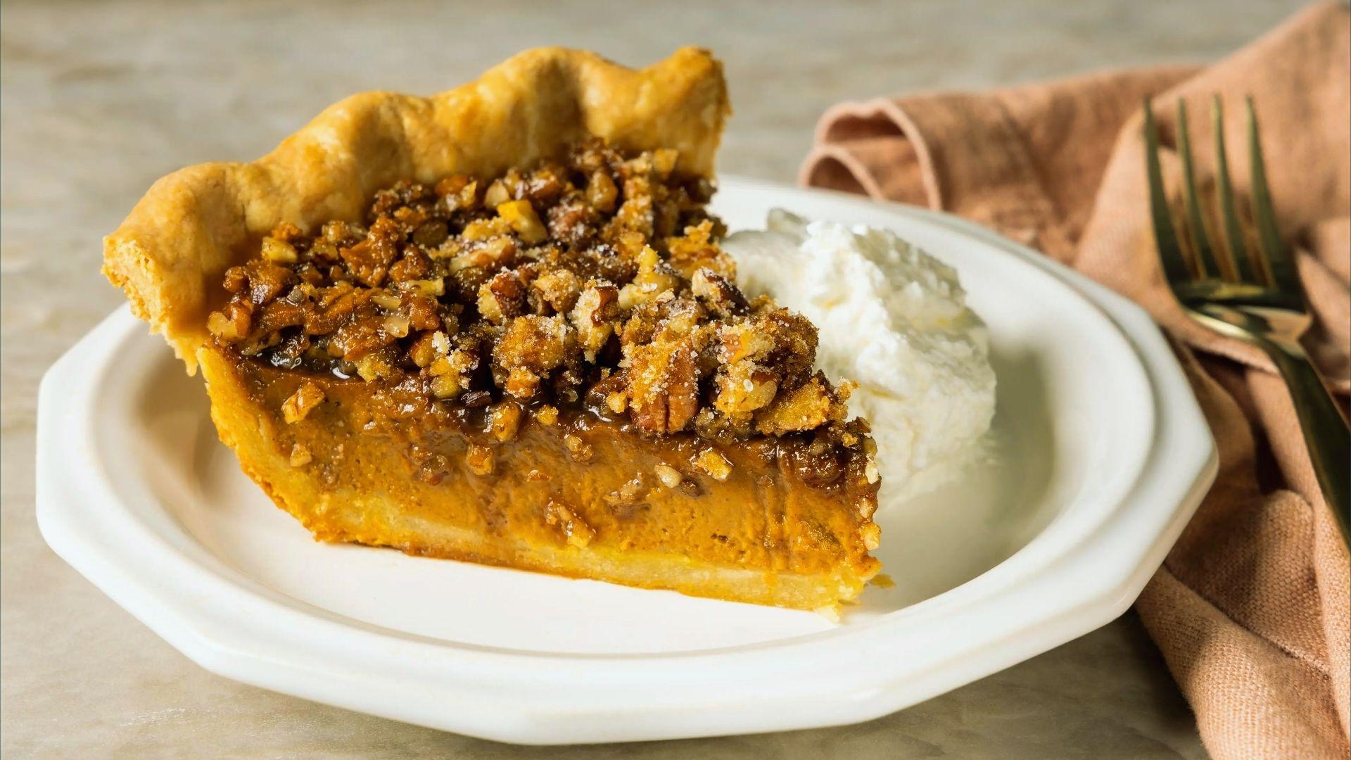 Slice of pecan pumpkin pie with whipped cream dollop on white plate